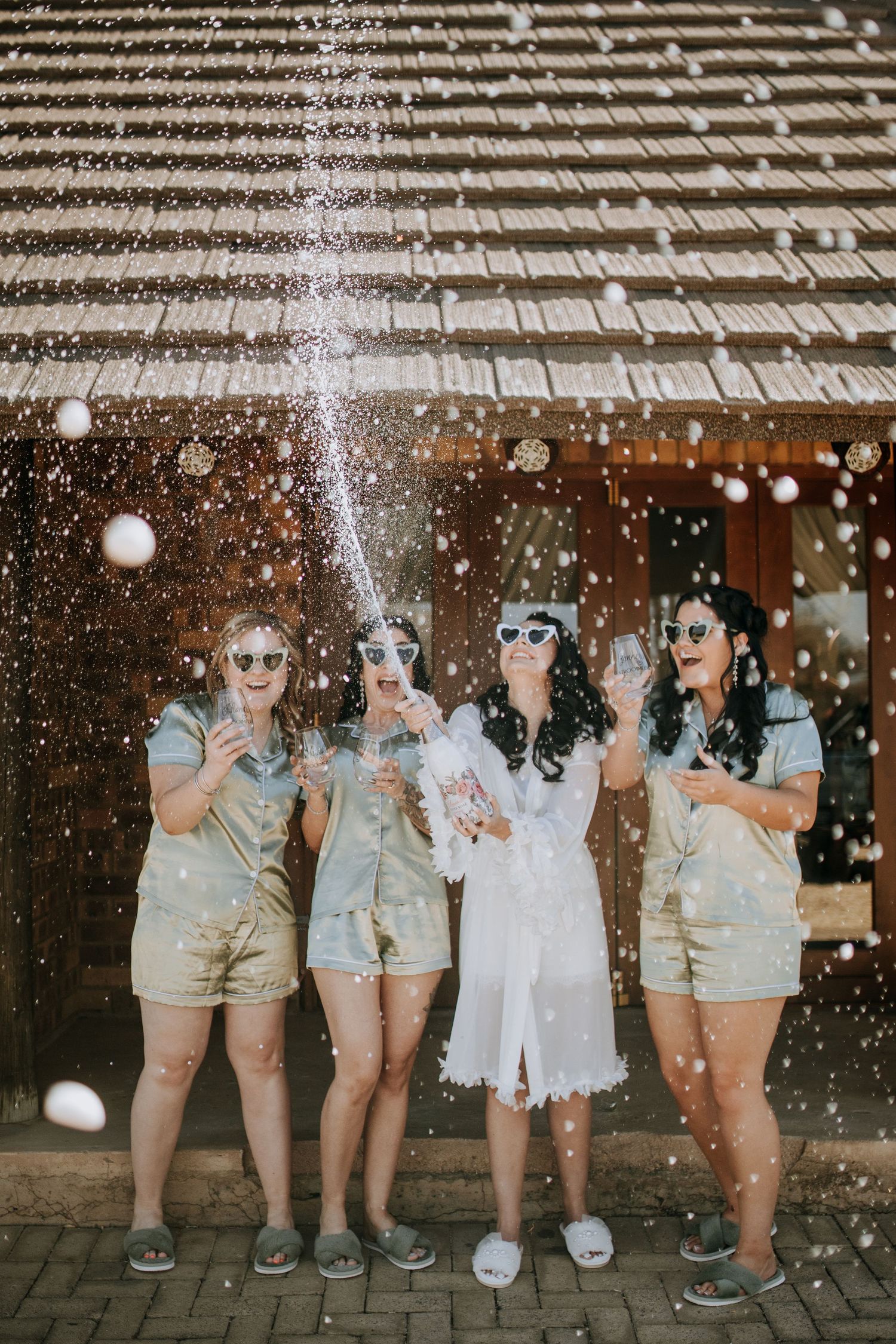Group wearing matching tan colored outfits poses against wall with sparkly bubbles and confetti effect in fun party scene.
