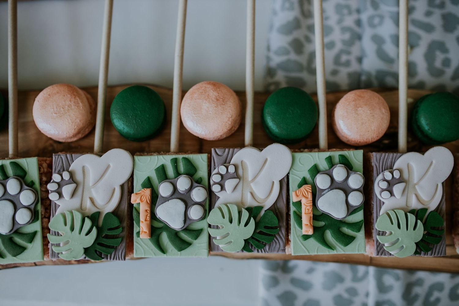 Wooden drawer filled with alternating pink and green macaron cookies beside paw print pattern decorative tiles.