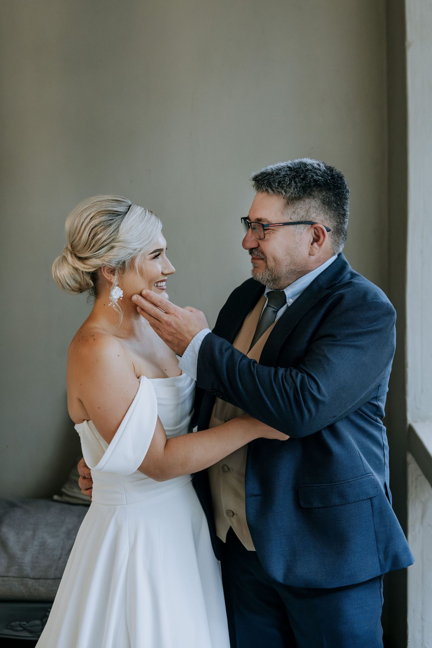 A tender moment between a couple on their wedding day, with the bride in white and groom in navy suit sharing a joyful laugh.