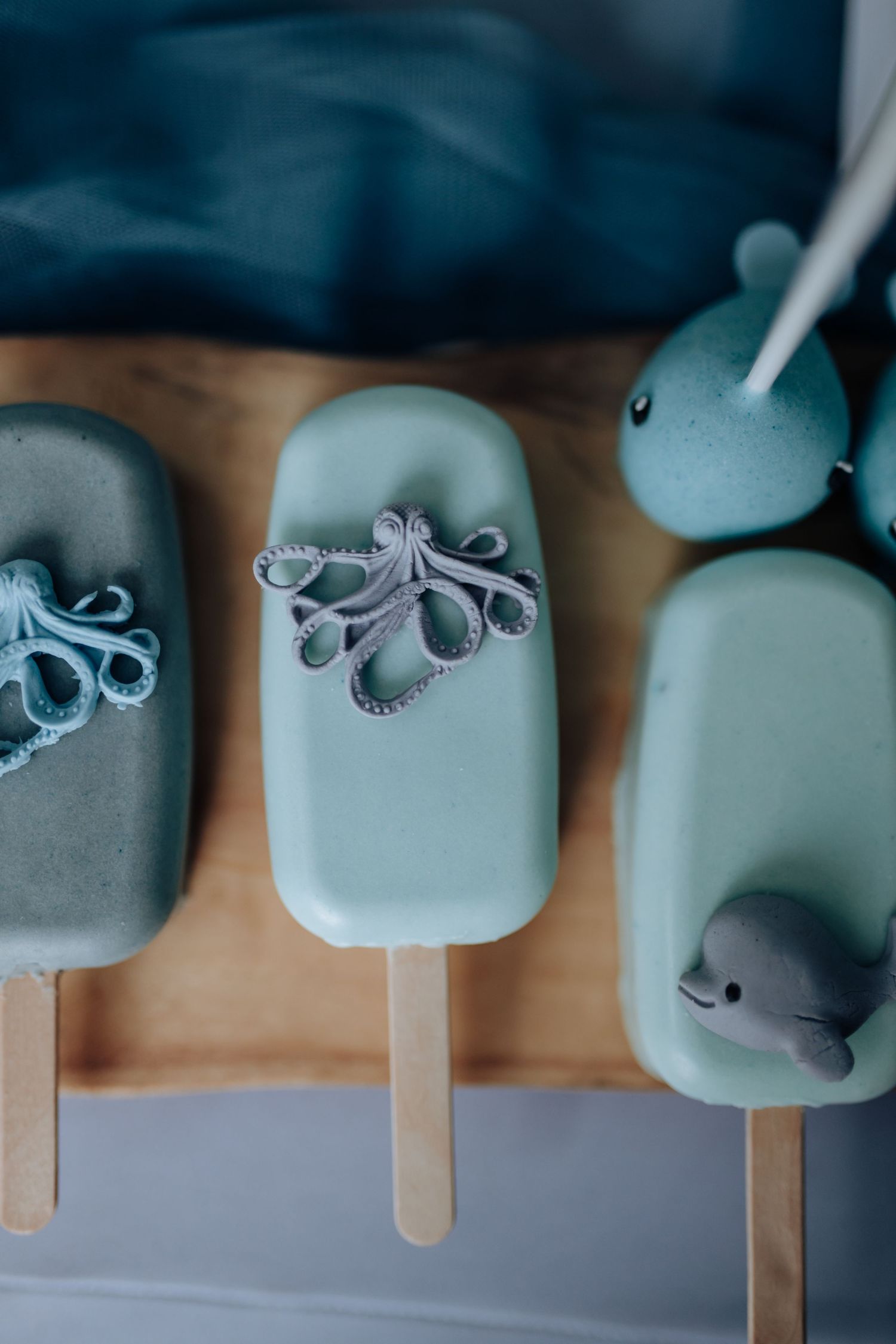 Blue and grey octopus cake pops lined up on wooden sticks against a light blue background.