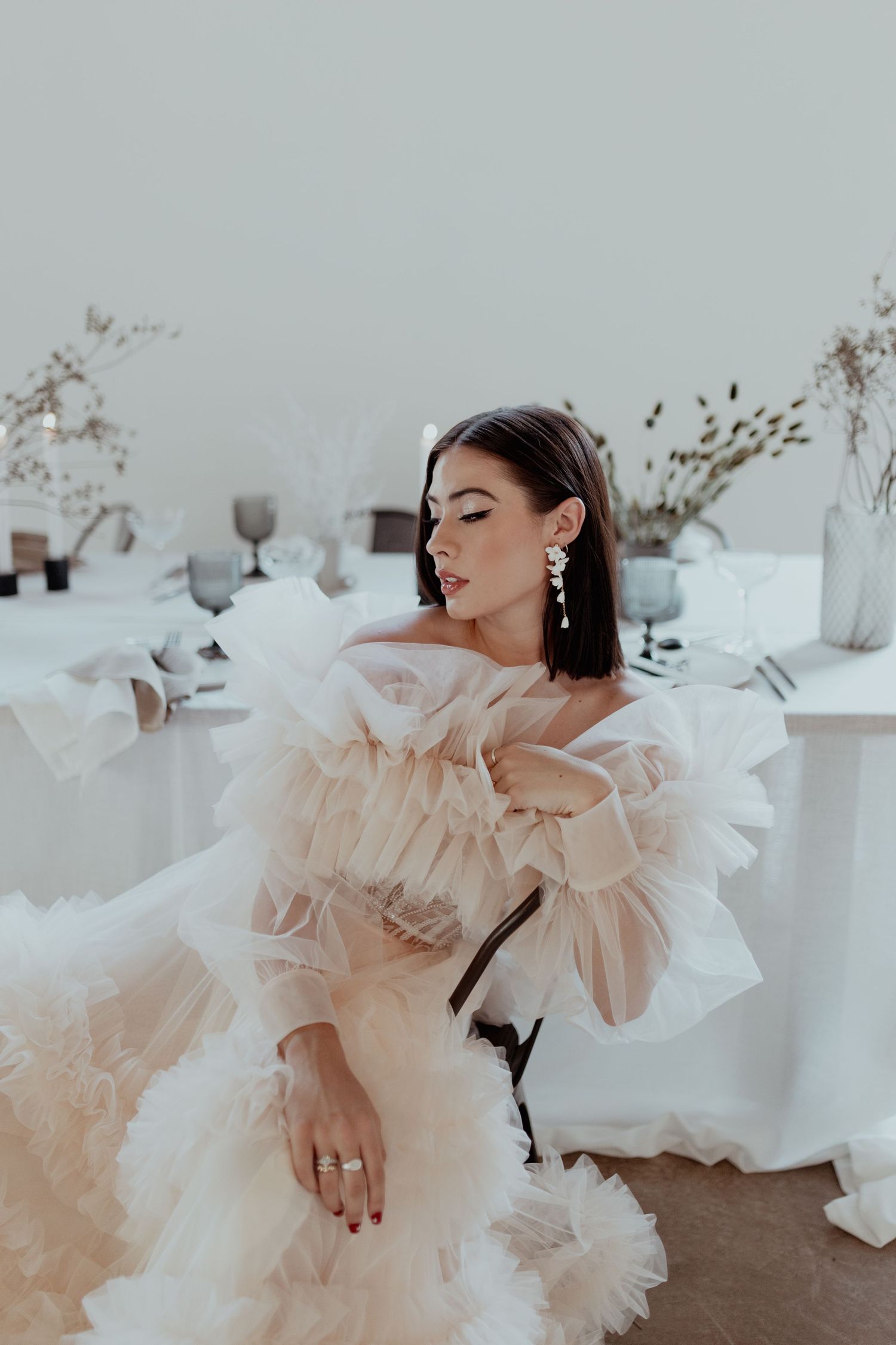 A person reclines in a dramatic white tulle gown with ruffled details set against a minimalist interior setting.