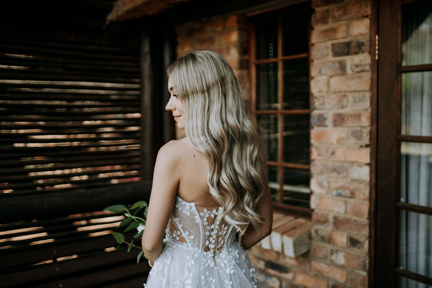 A stylish backless beaded gown with delicate sequin details sparkles in natural lighting against a rustic brick wall.