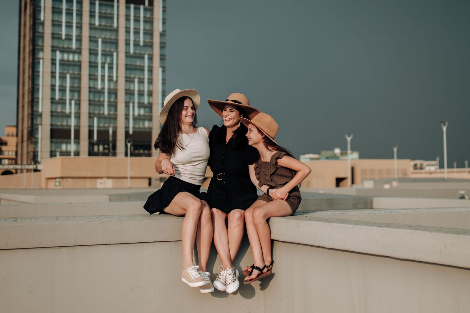 Two people sitting on an outdoor concrete ledge under moody blue skies near modern high-rise buildings.