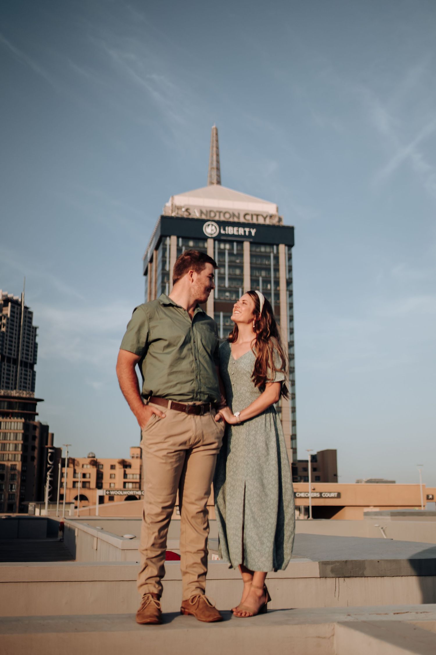 Romantic couple share an intimate moment on a city rooftop with urban skyline views at golden hour.