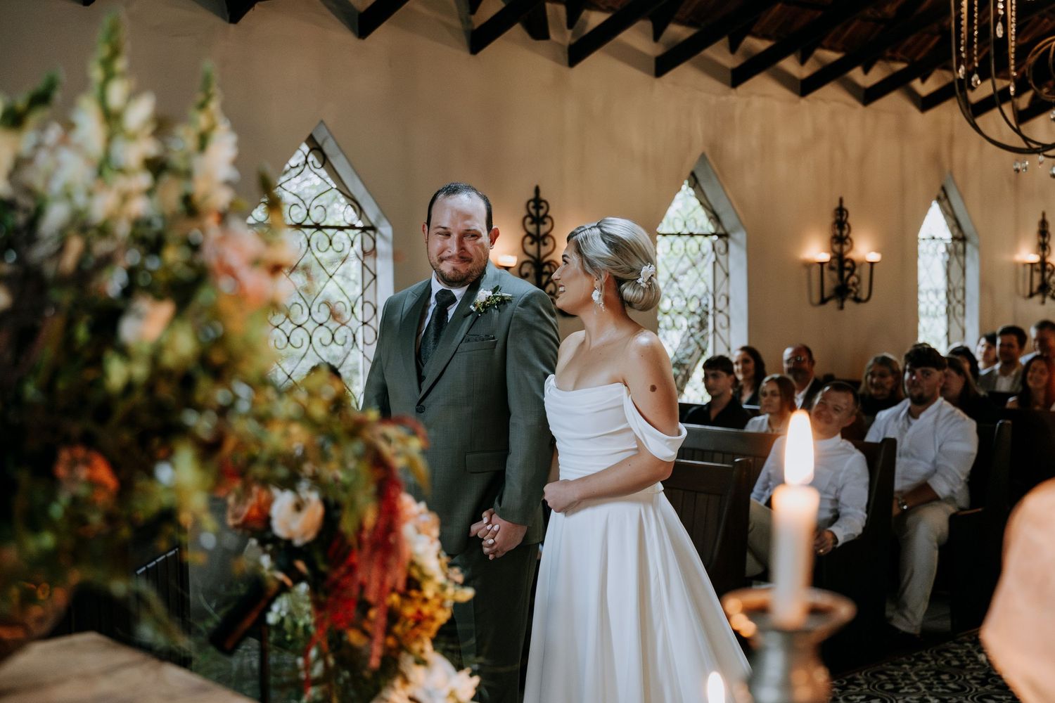 A couple shares a romantic moment during their wedding ceremony in an elegant church with stained glass windows.