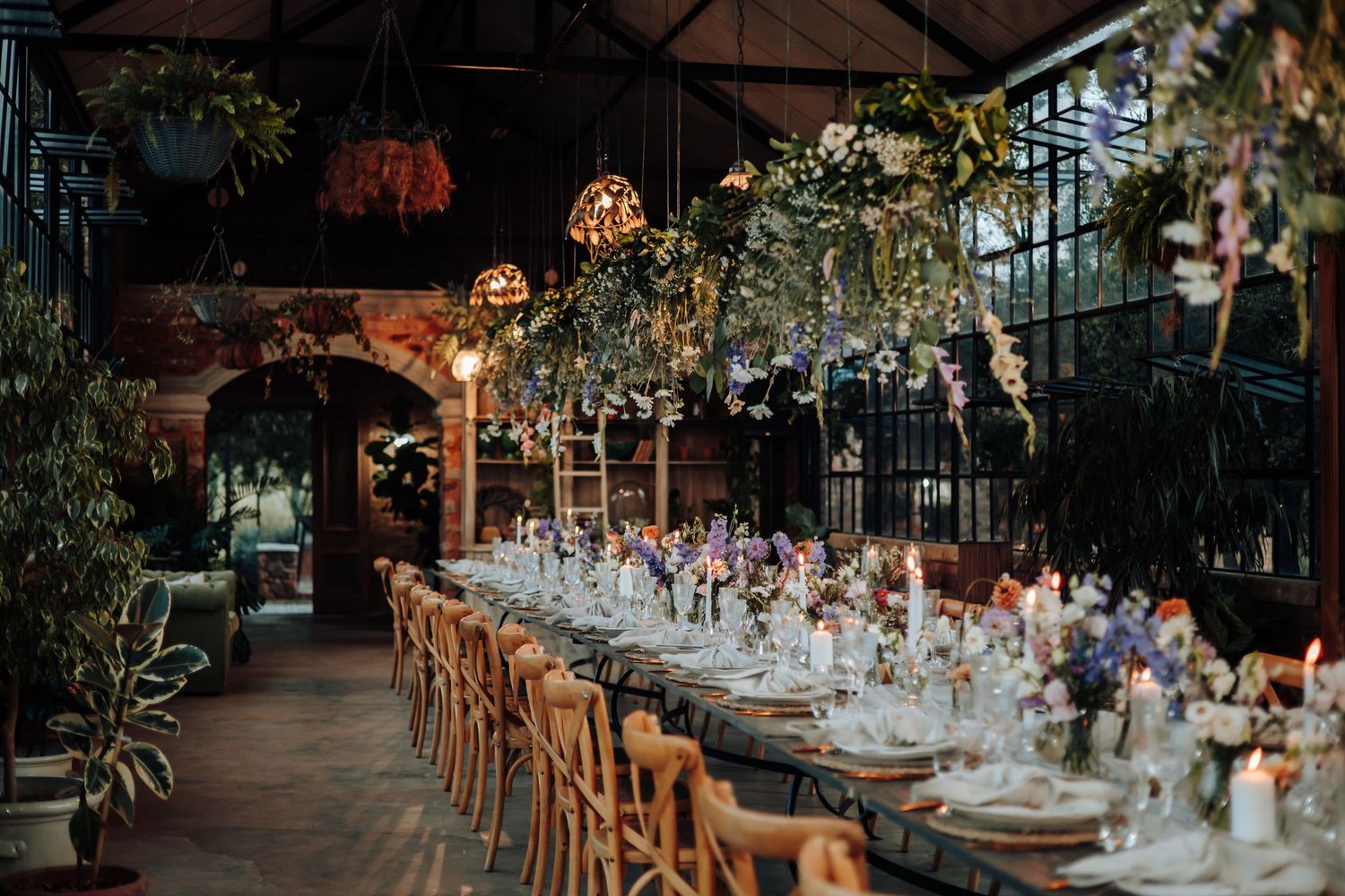 Long wooden tables adorned with elegant place settings and floral centerpieces under twinkling lights at an outdoor reception.