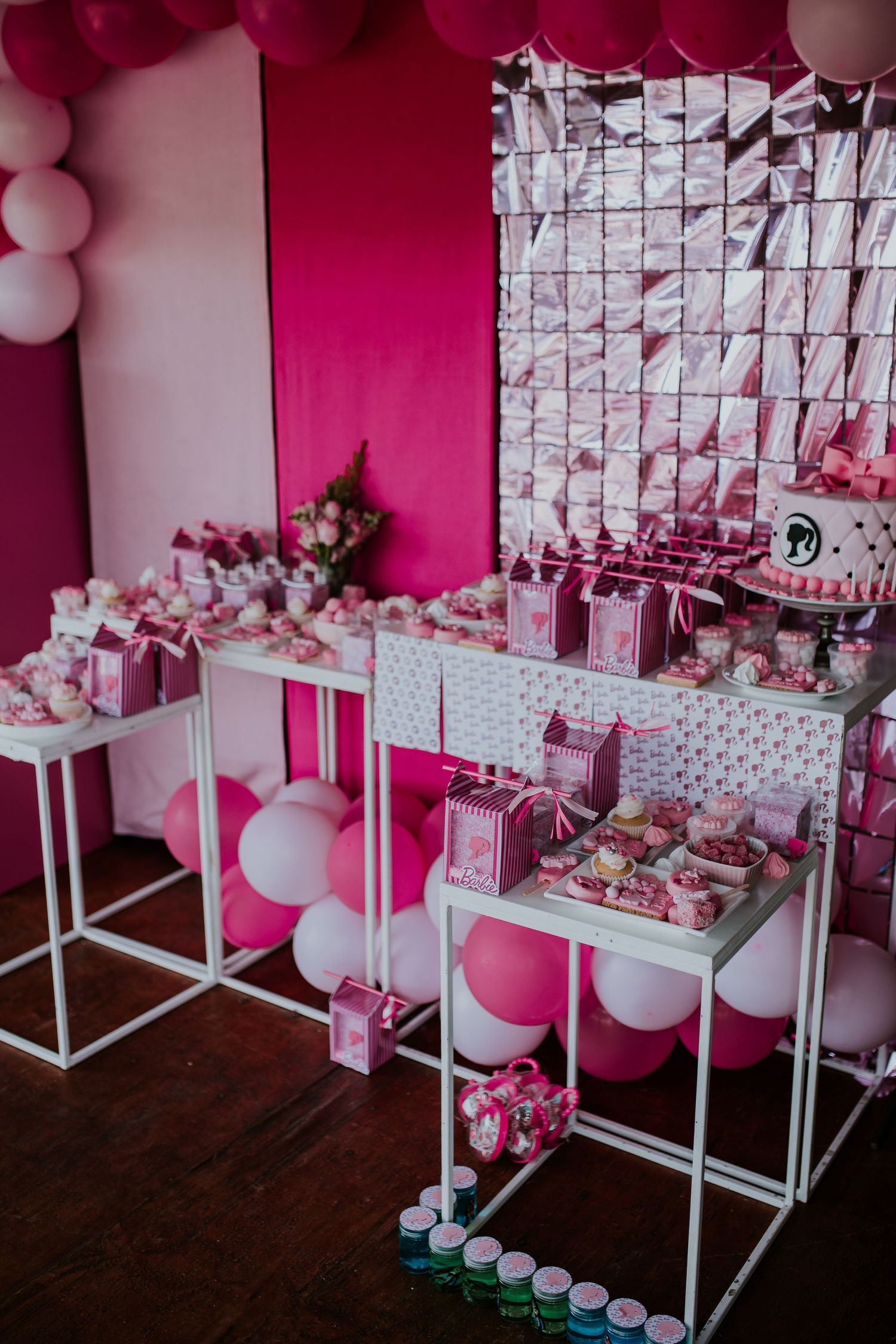Pink and white themed party decoration setup with balloon garlands and dessert display tables arranged against white backdrop.