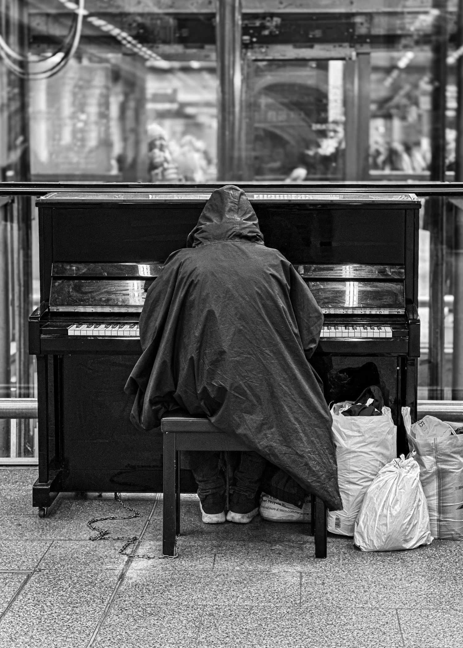 A hooded figure plays the piano at London St Pancras.