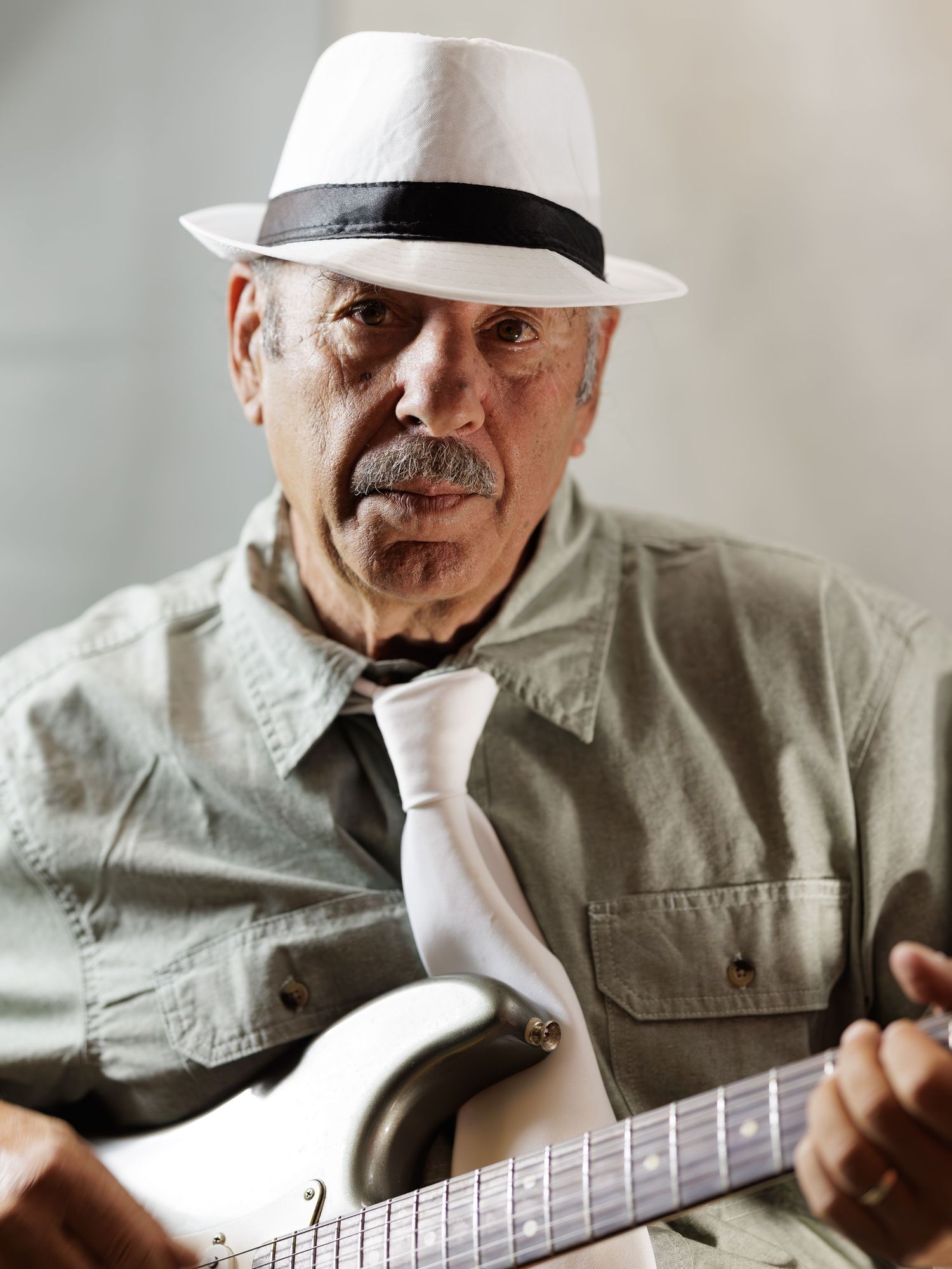 A musician in a white hat plays an acoustic guitar in a soft-lit studio setting.