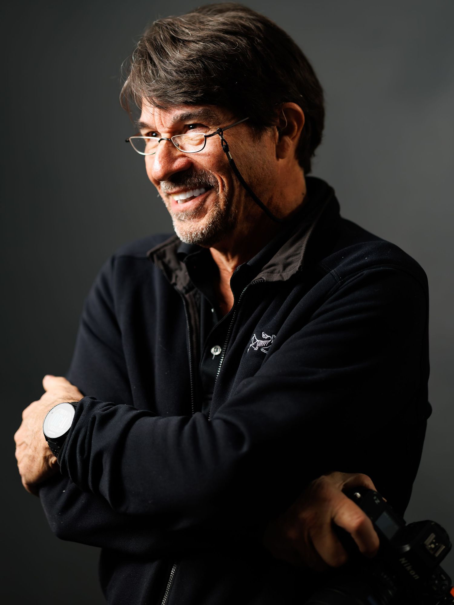 A person wearing a black sweater and glasses poses expressively against a dark background in a photo series.