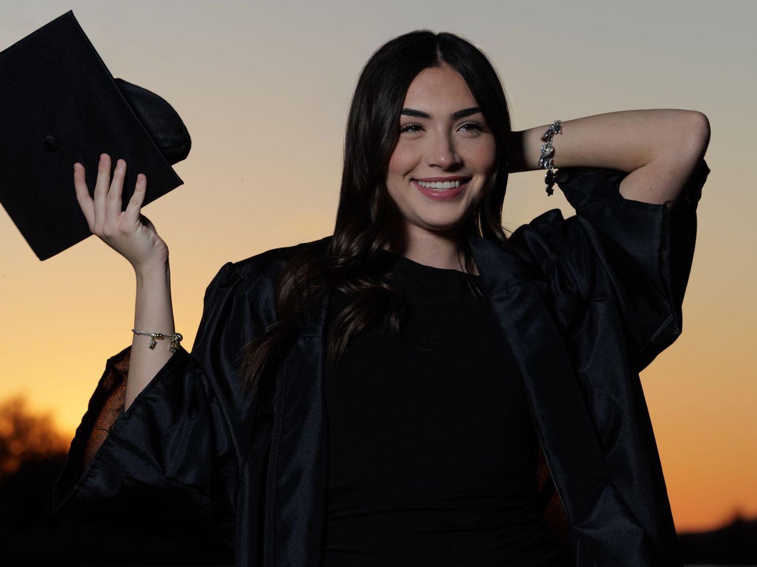 Silhouettes of graduates in caps and gowns throwing their mortarboards into the air at sunset.