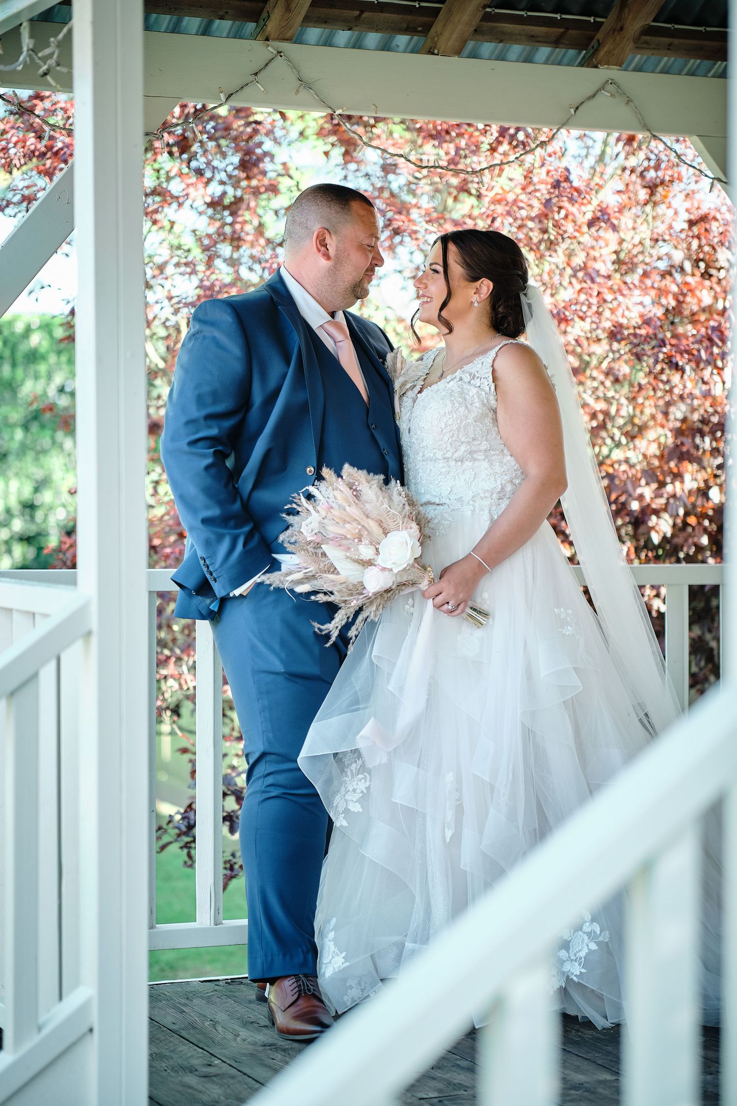 A romantic wedding portrait under a gazebo with blooming cherry blossoms in the background.