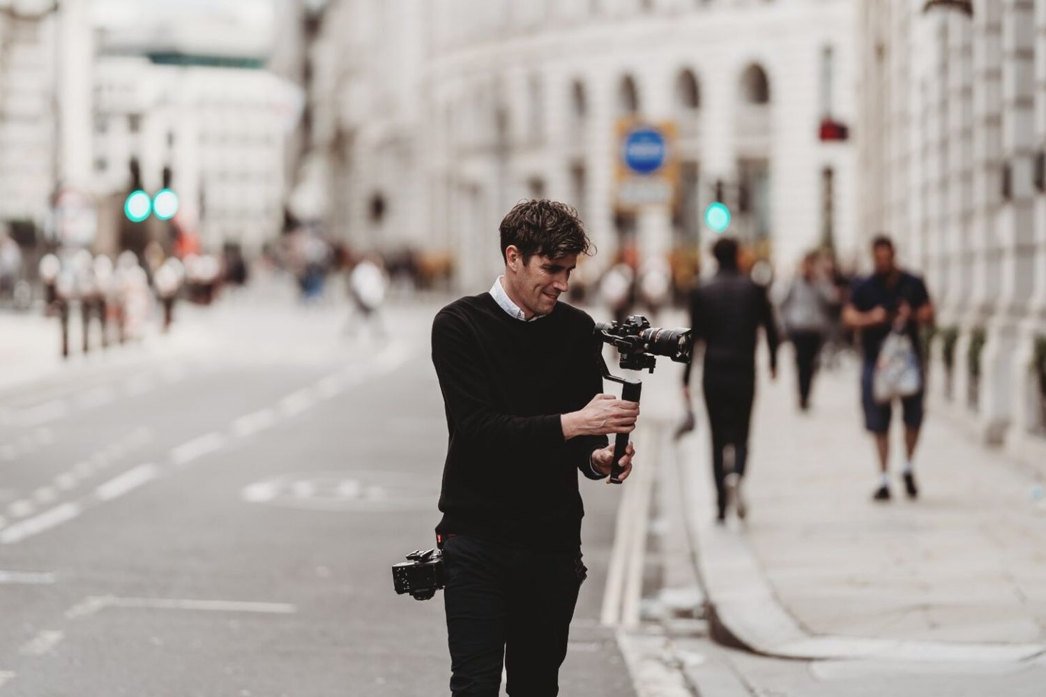 Professional photographer wearing all black using camera equipment on a city street.