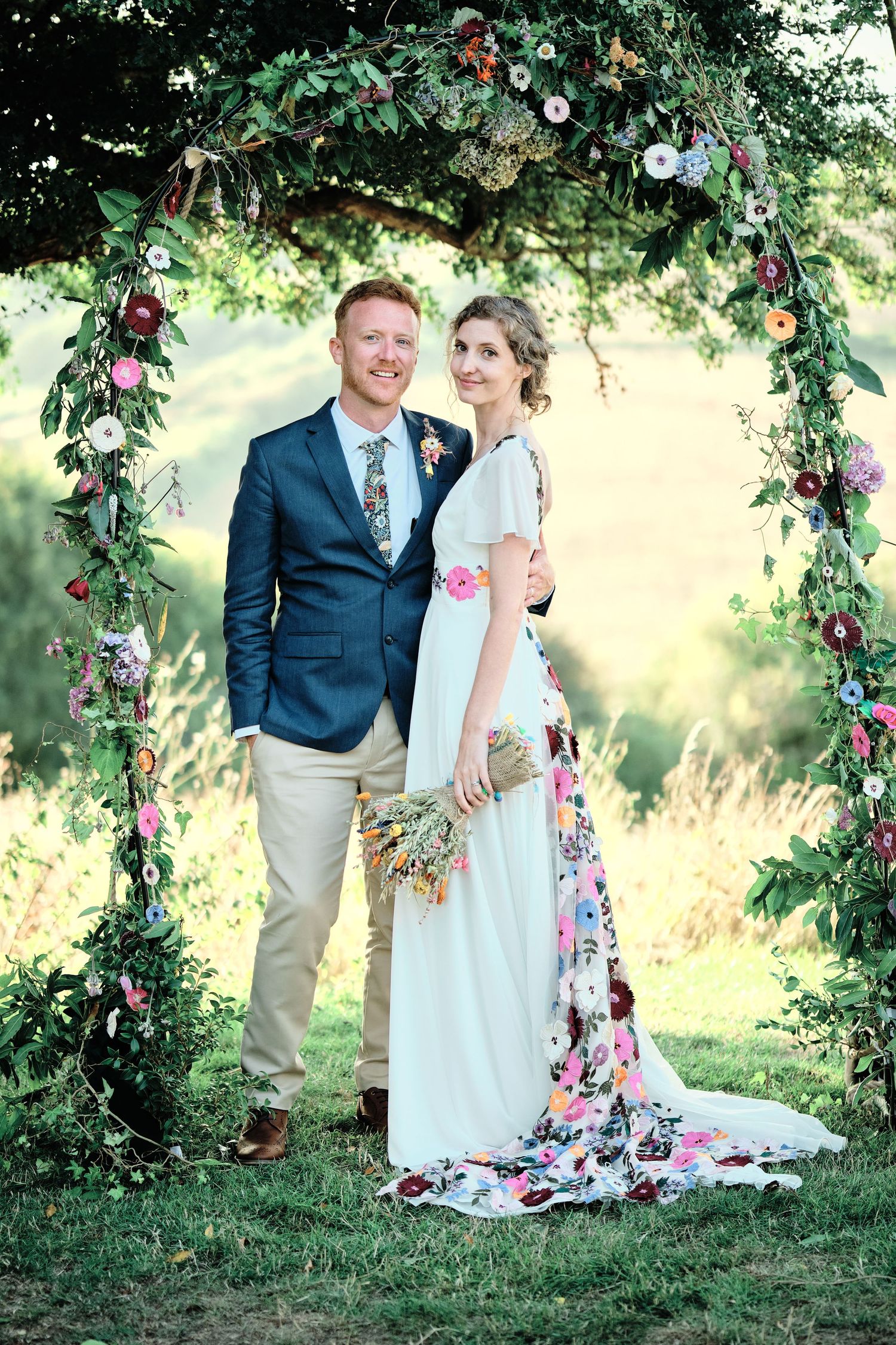 A romantic outdoor wedding photo series with a couple posing under a floral arch in a garden setting.