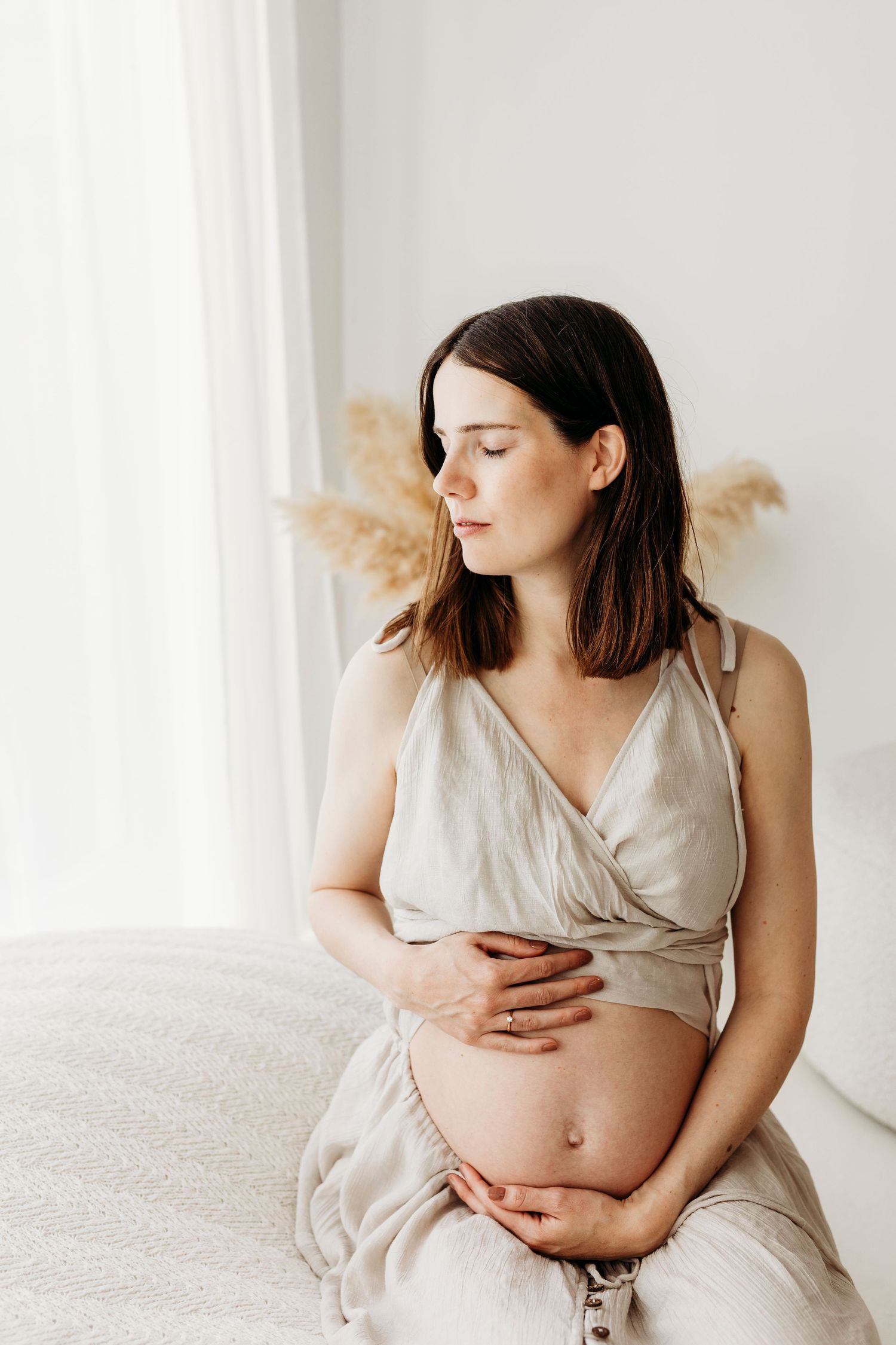 Intieme zwangerschapsfotografie van een moeder in een lichte studio met natuurlijke tinten en rust.