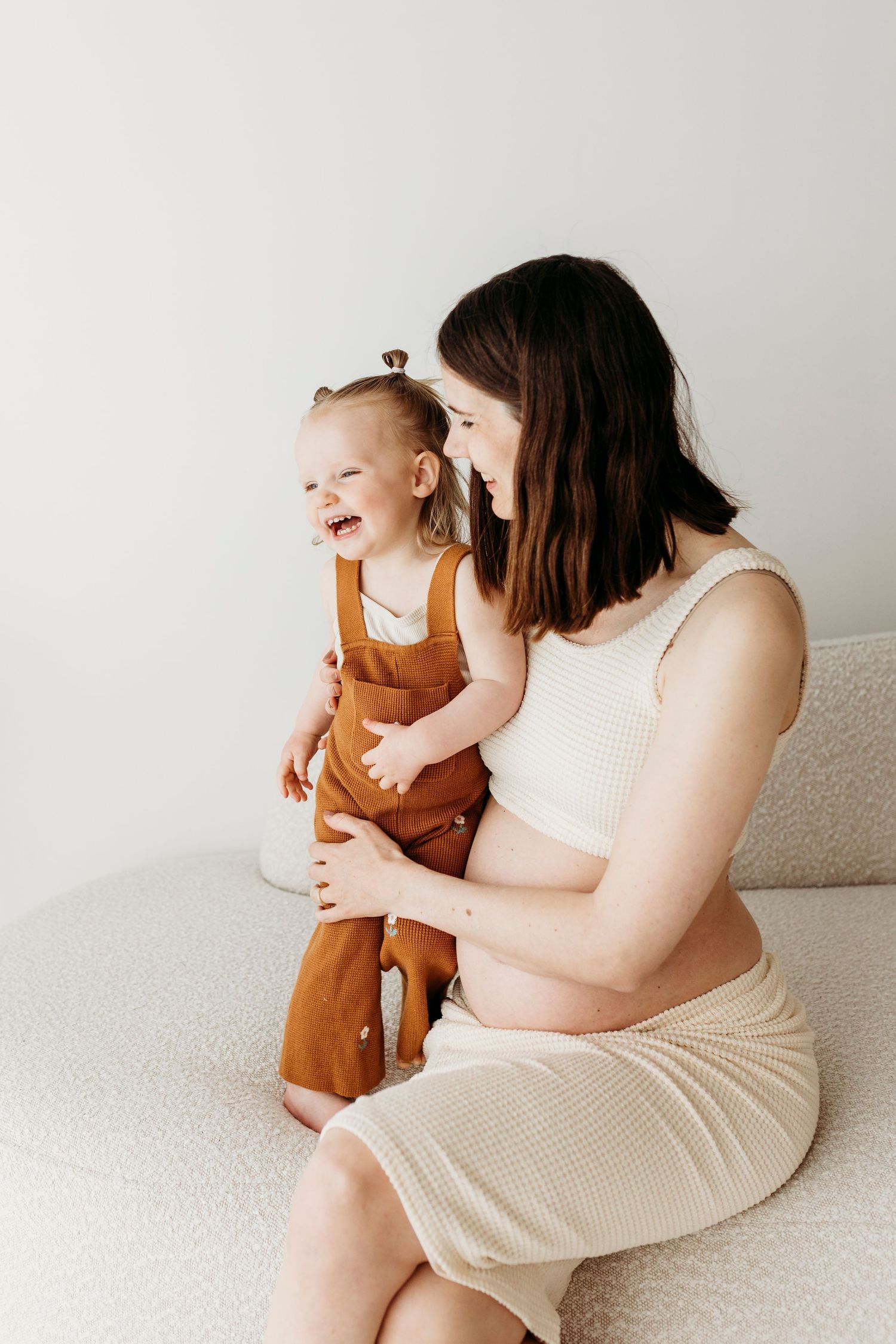 mama en dochter zwangerschapstoot in de lichte studio in Soest meisje lacht en mama houdt haar vast