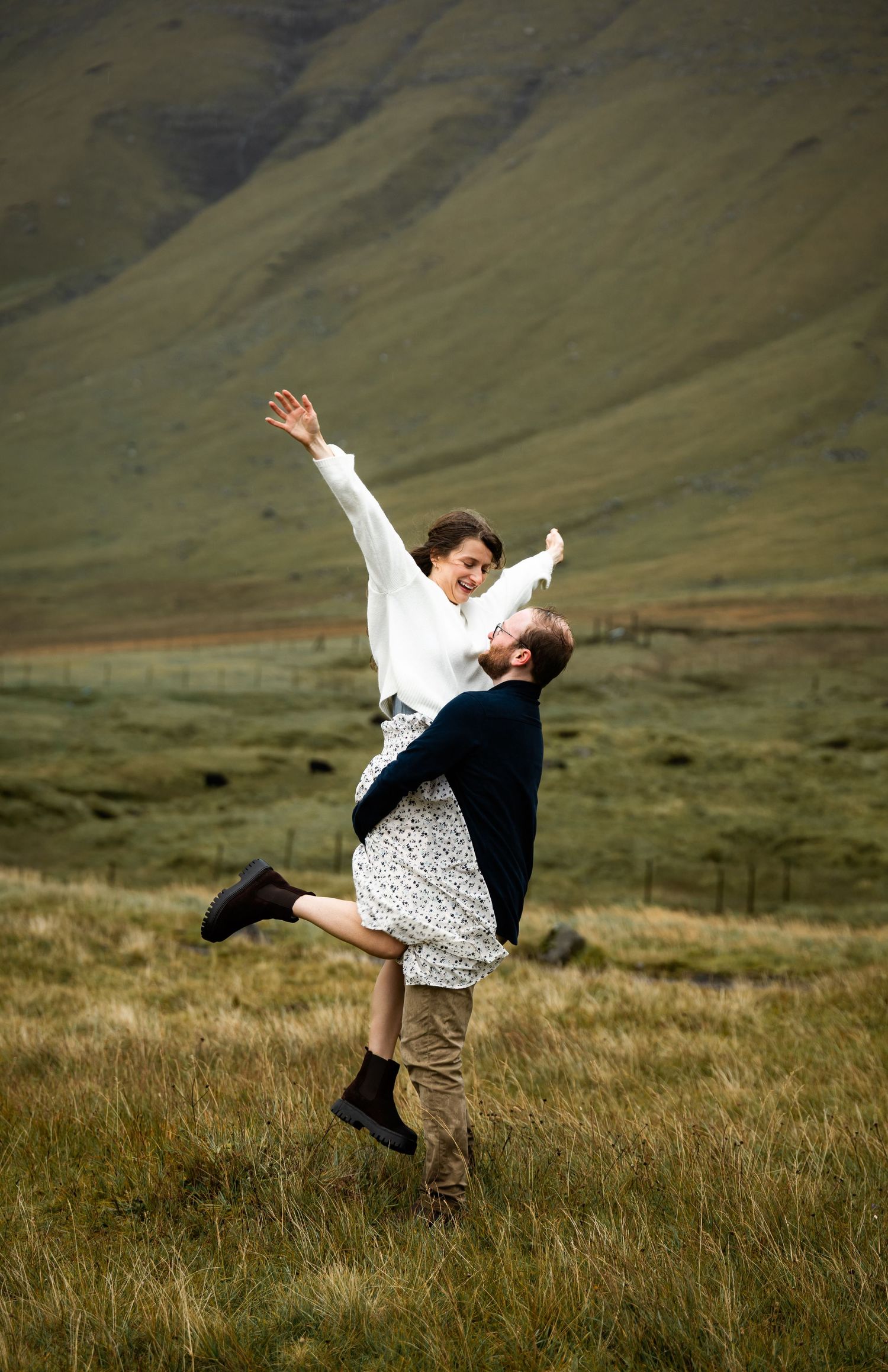 Two dancers perform a graceful lift in a scenic mountain meadow with rolling green hills in the background.