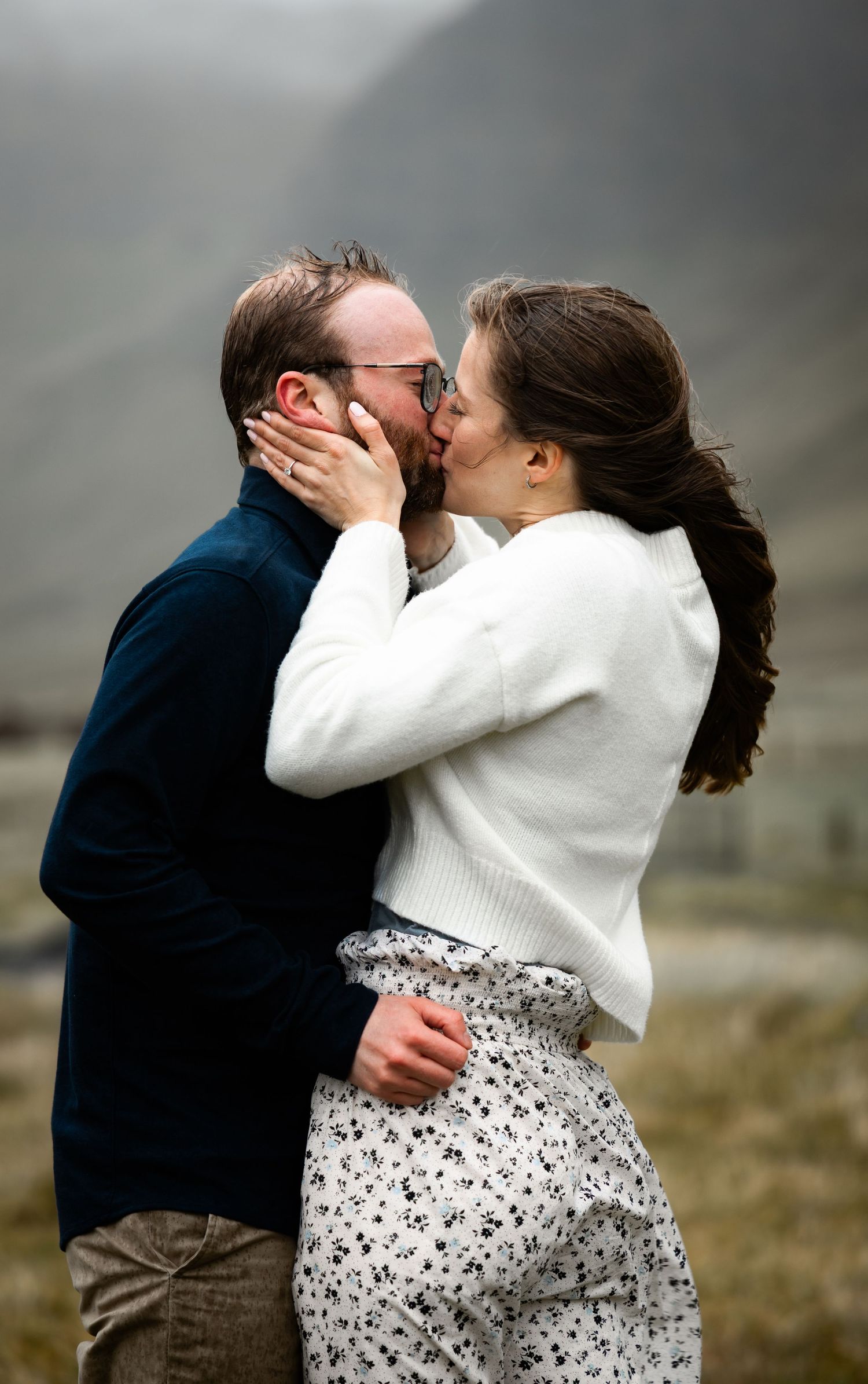 A romantic couple embraces and kisses outdoors in a series of tender moments, with the woman wearing a white sweater and patterned skirt.