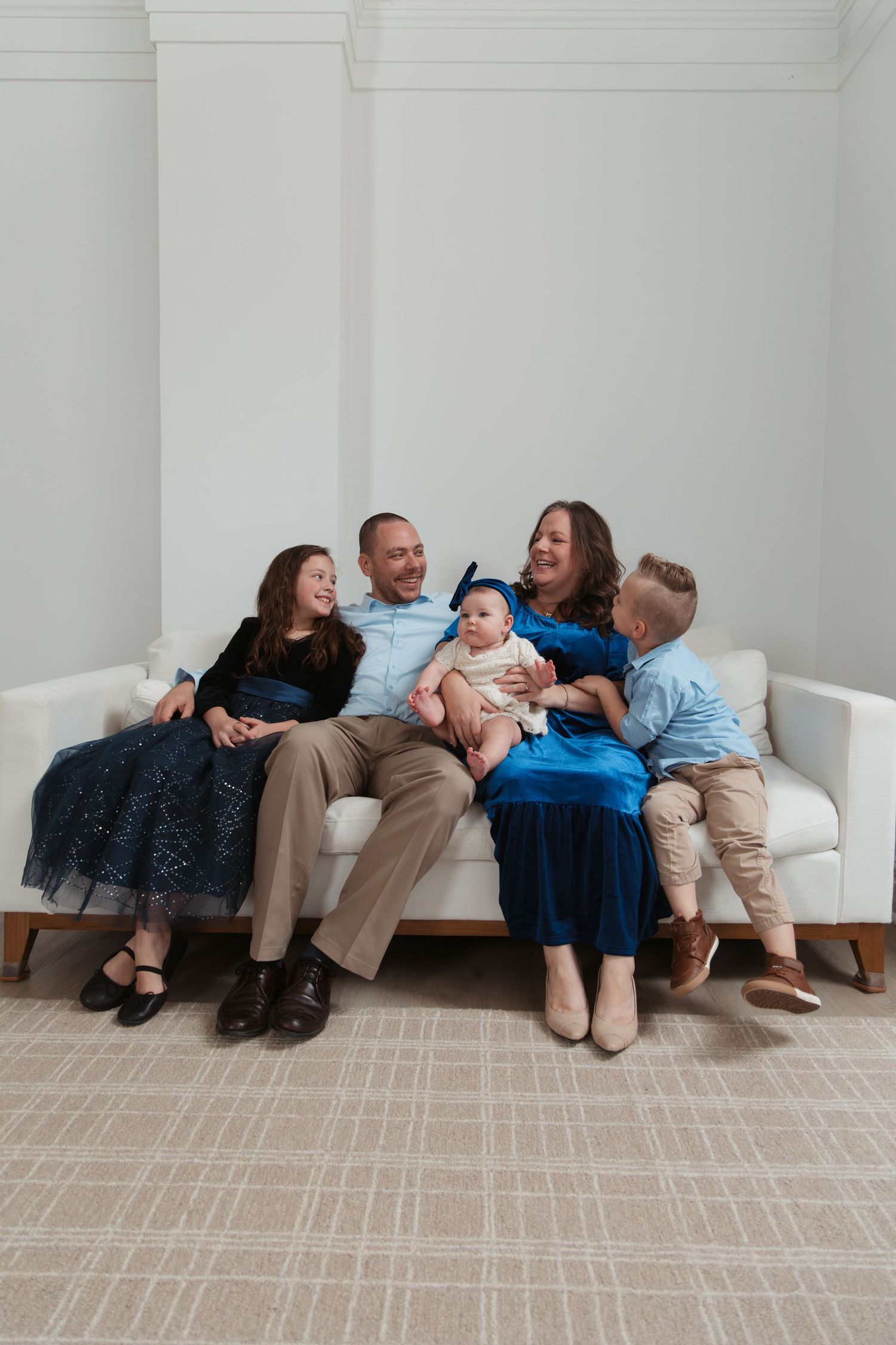 A family shares a joyful moment together while sitting on a white couch against a minimalist white wall background.