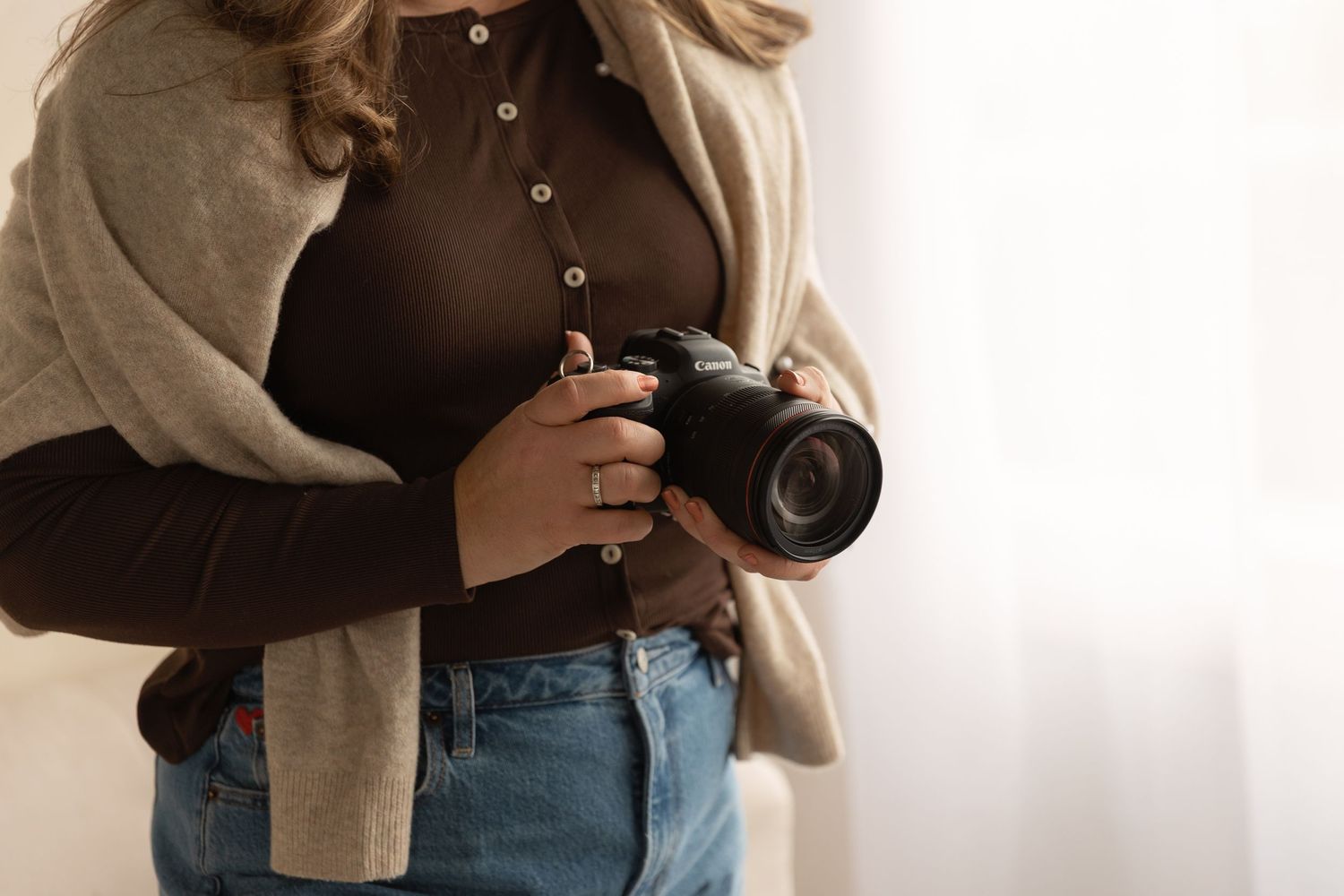 Close-up shot of photographer's torso holding camera wearing brown top and beige cardigan.