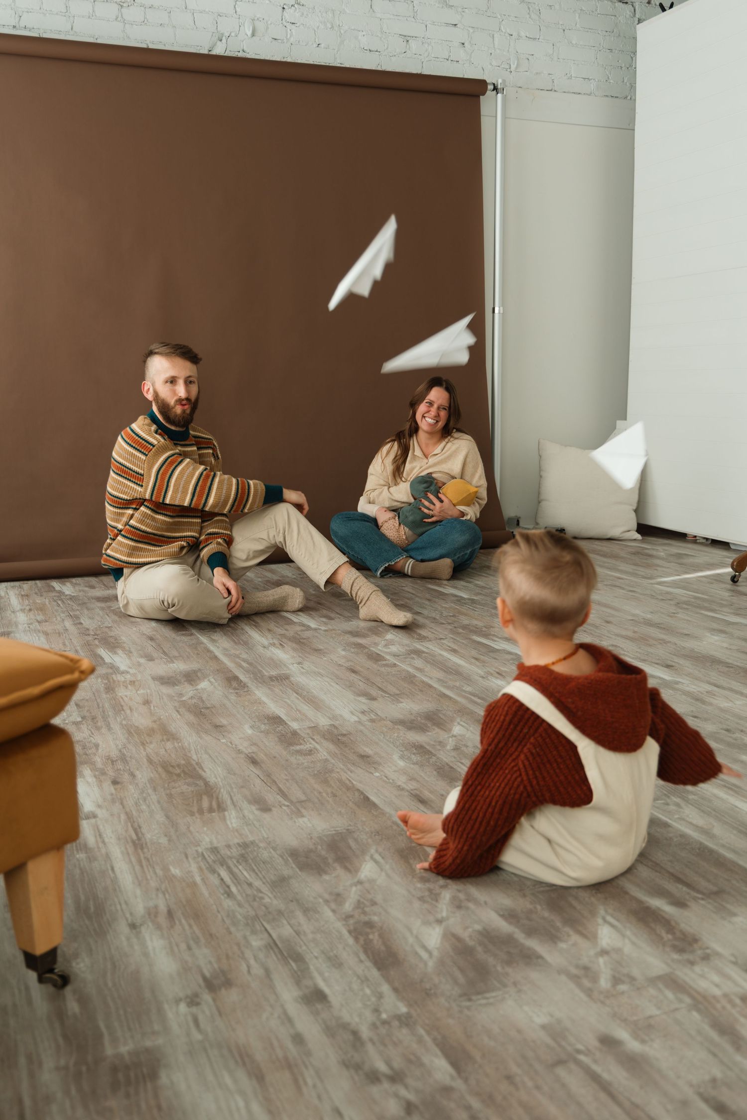 People tossing paper airplanes while sitting on hardwood floor in minimalist white room.