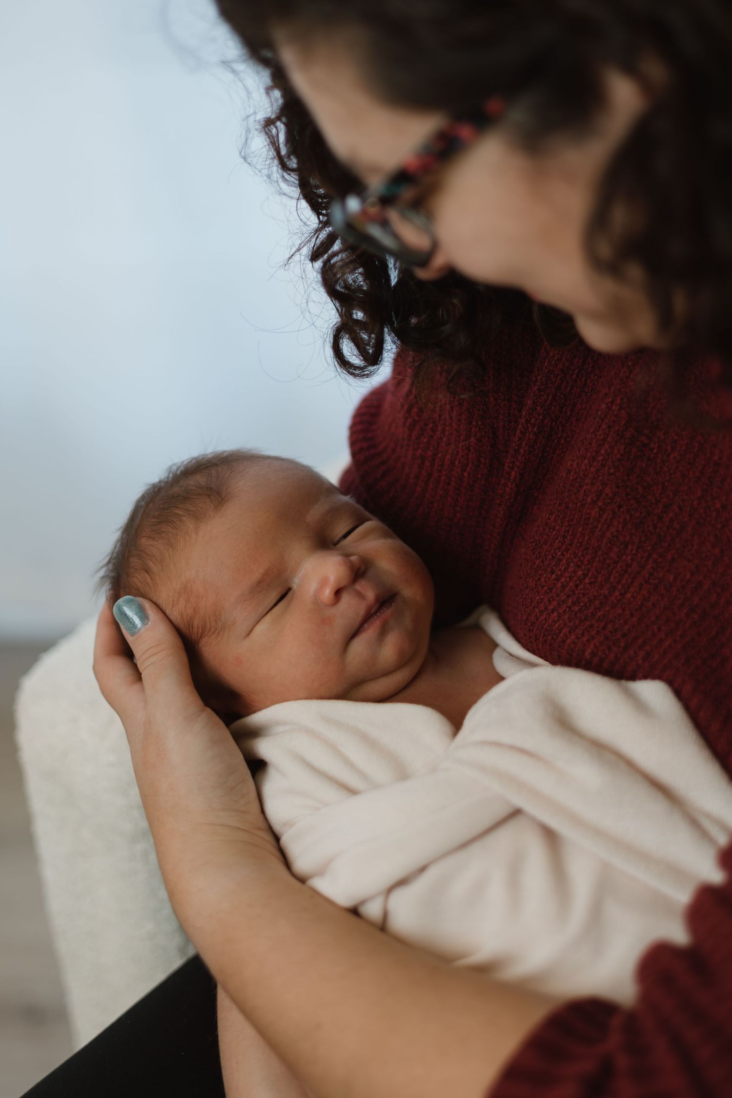 Parent in burgundy sweater holding and comforting sleeping newborn baby in swaddle.