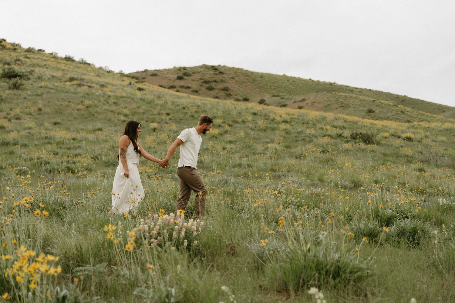 Two people walk hand in hand through a wildflower-dotted hillside in spring.