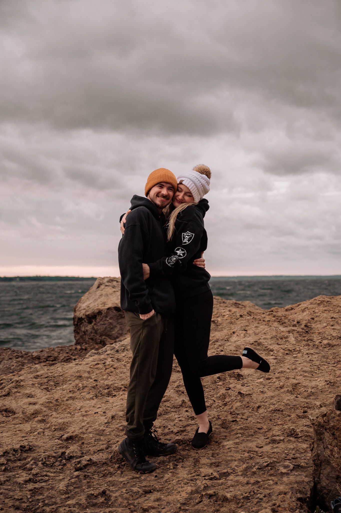 Jon and Heather Penton, the married photo team, share an intimate moment on a rocky cliff overlooking a dramatic cloudy seascape at sunset.