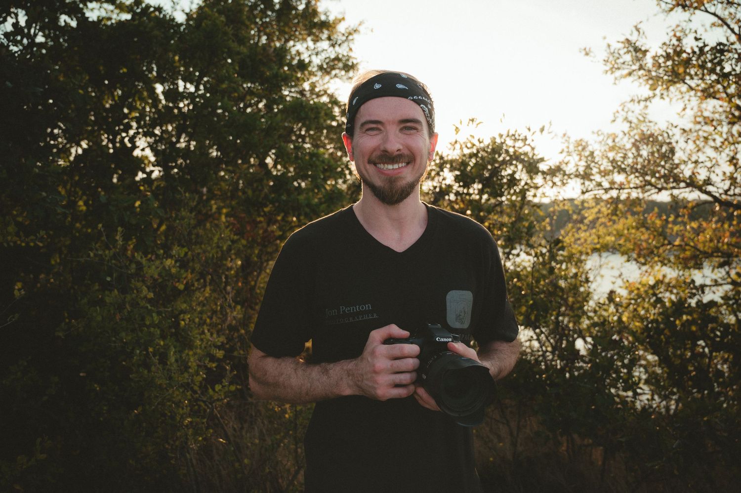 Person enjoying a beverage outdoors at sunset with trees and natural lighting in the background.