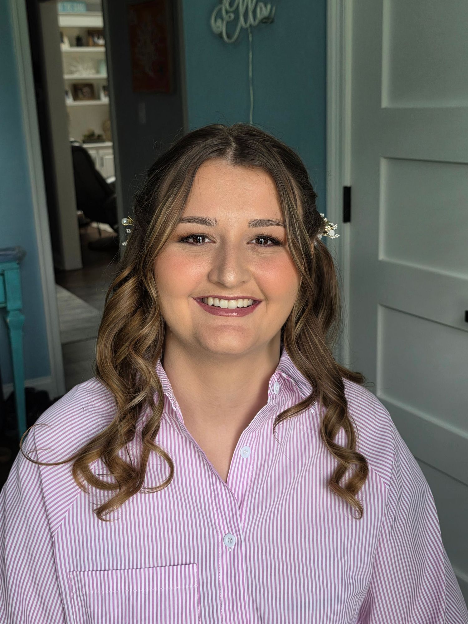 Person wearing a pink striped button-down shirt with styled wavy brown hair.