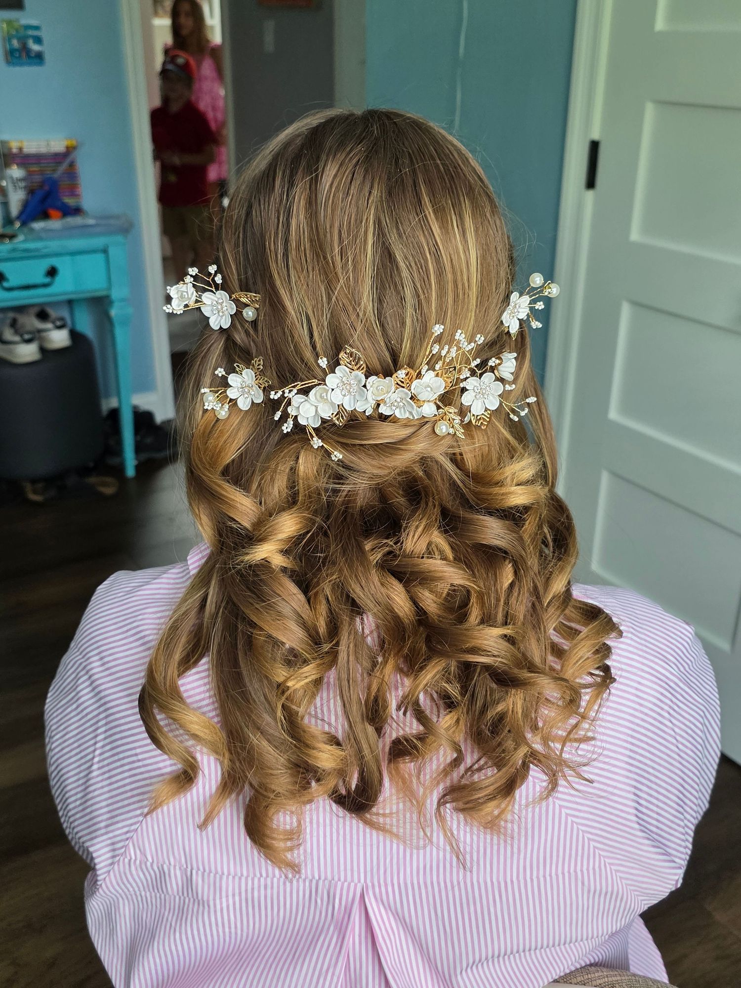 Back view of bridal half-up hairstyle with loose curls and white floral hair vine accessory.