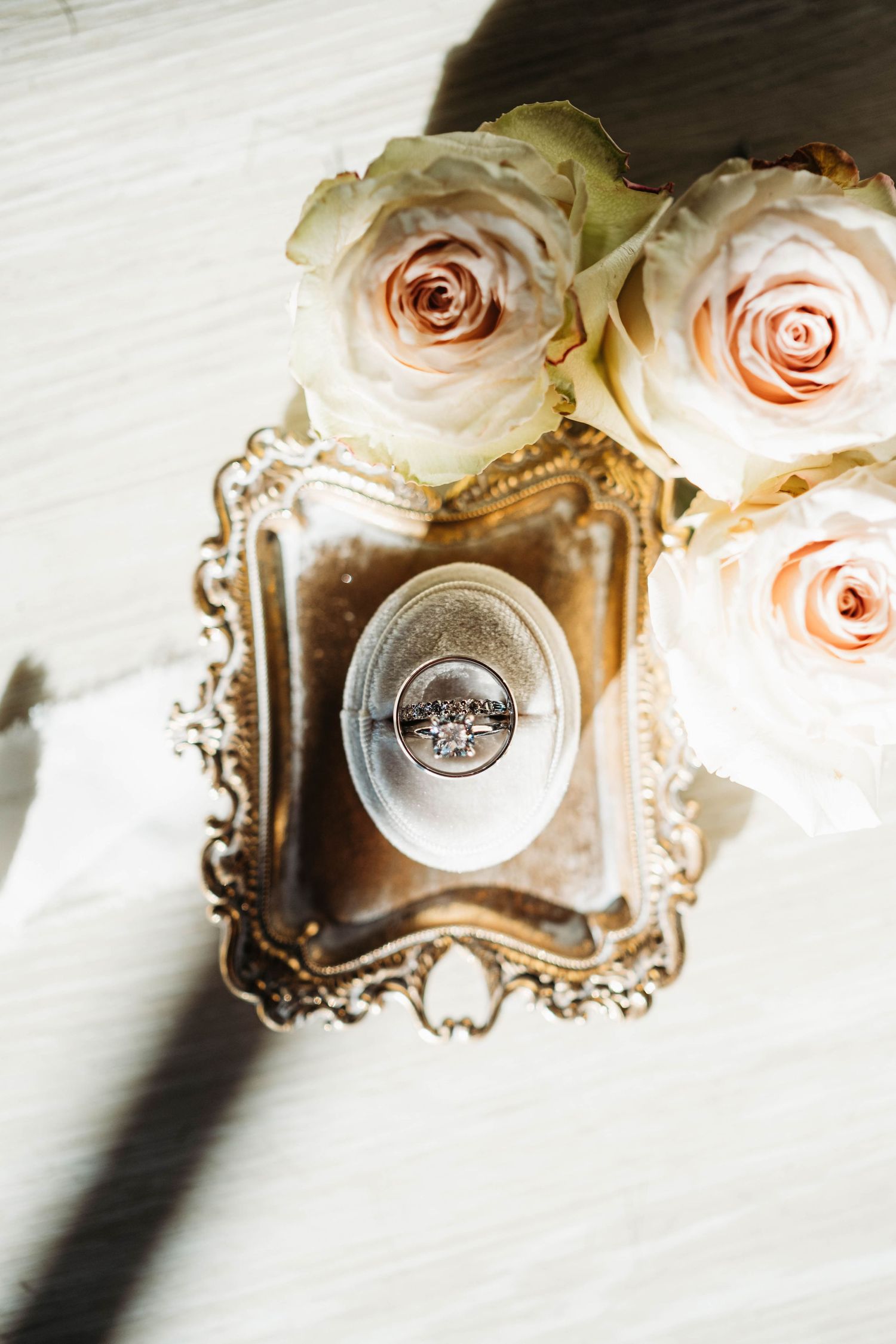 Elegant wedding rings displayed on vintage ornate tray with soft pink roses.