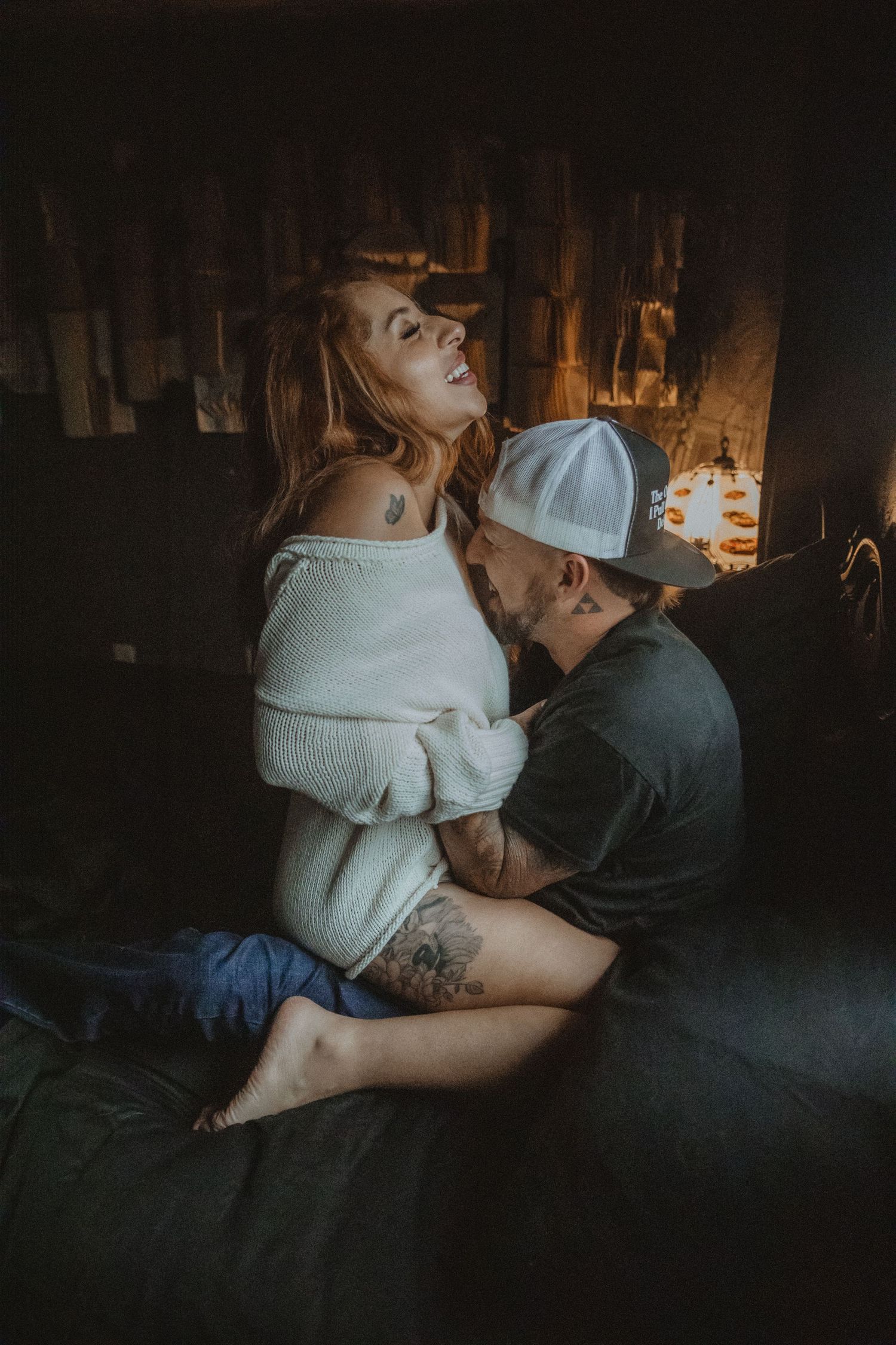 A couple embraces intimately in a dimly lit room wearing white and dark colored clothing. Tucson couples boudoir.