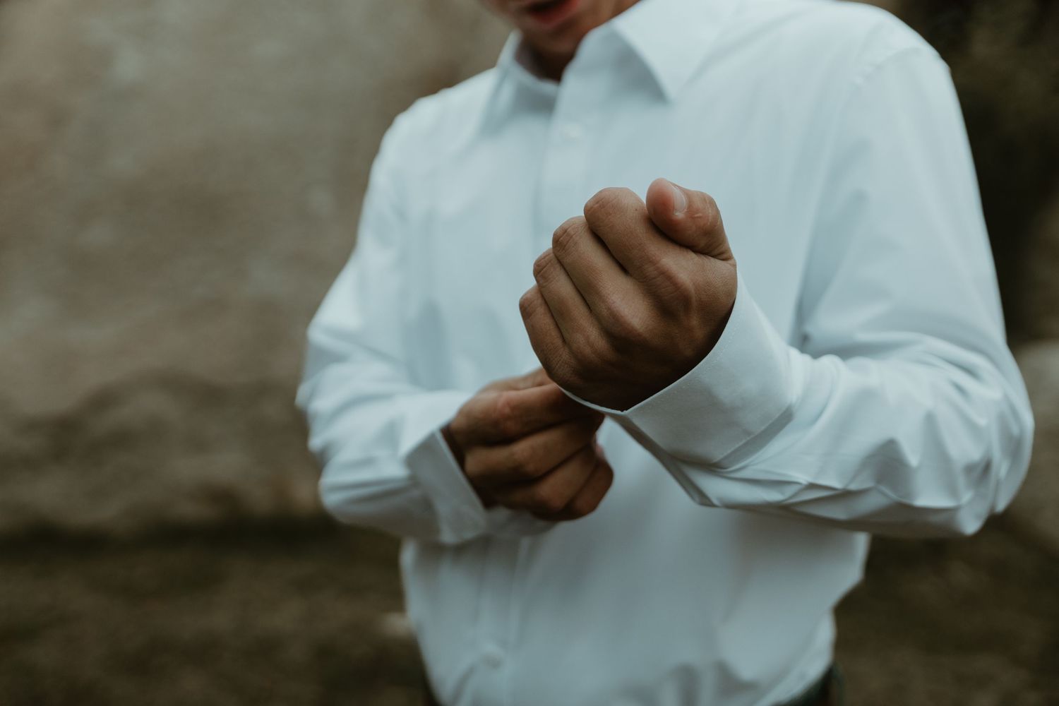 A person in a white button-up shirt holds a cup of coffee while standing against a dark background. Tucson Wedding photographer