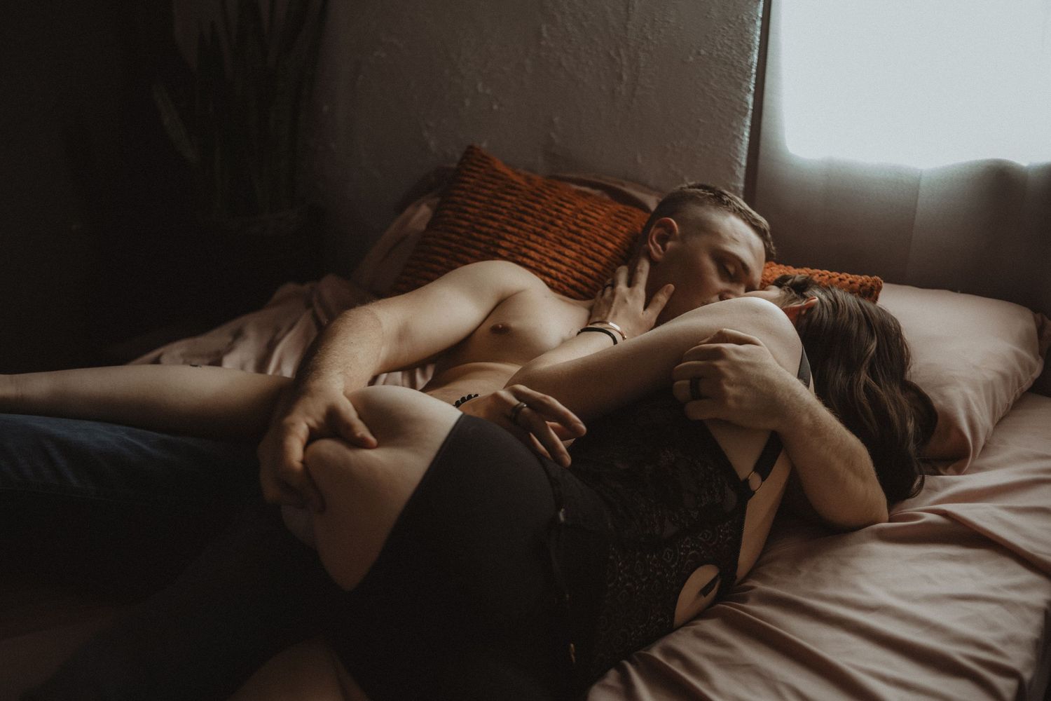 A person lies peacefully asleep in bed with soft morning light streaming through the window. Tucson couples boudoir.