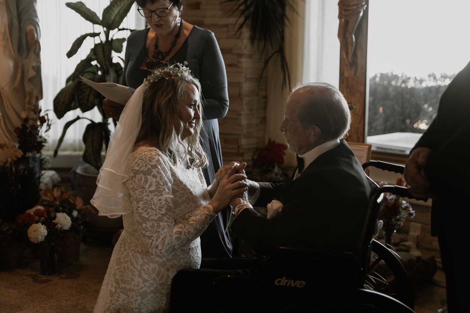 Intimate indoor elopement ceremony with officiant reading vows as the couple holds hands, surrounded by close family and warm natural light.