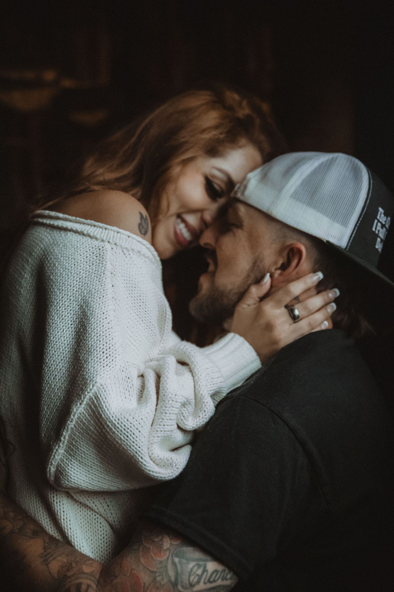 An intimate romantic moment between a couple embracing, with the woman in a white sweater and the man wearing a baseball cap. Tucson couples