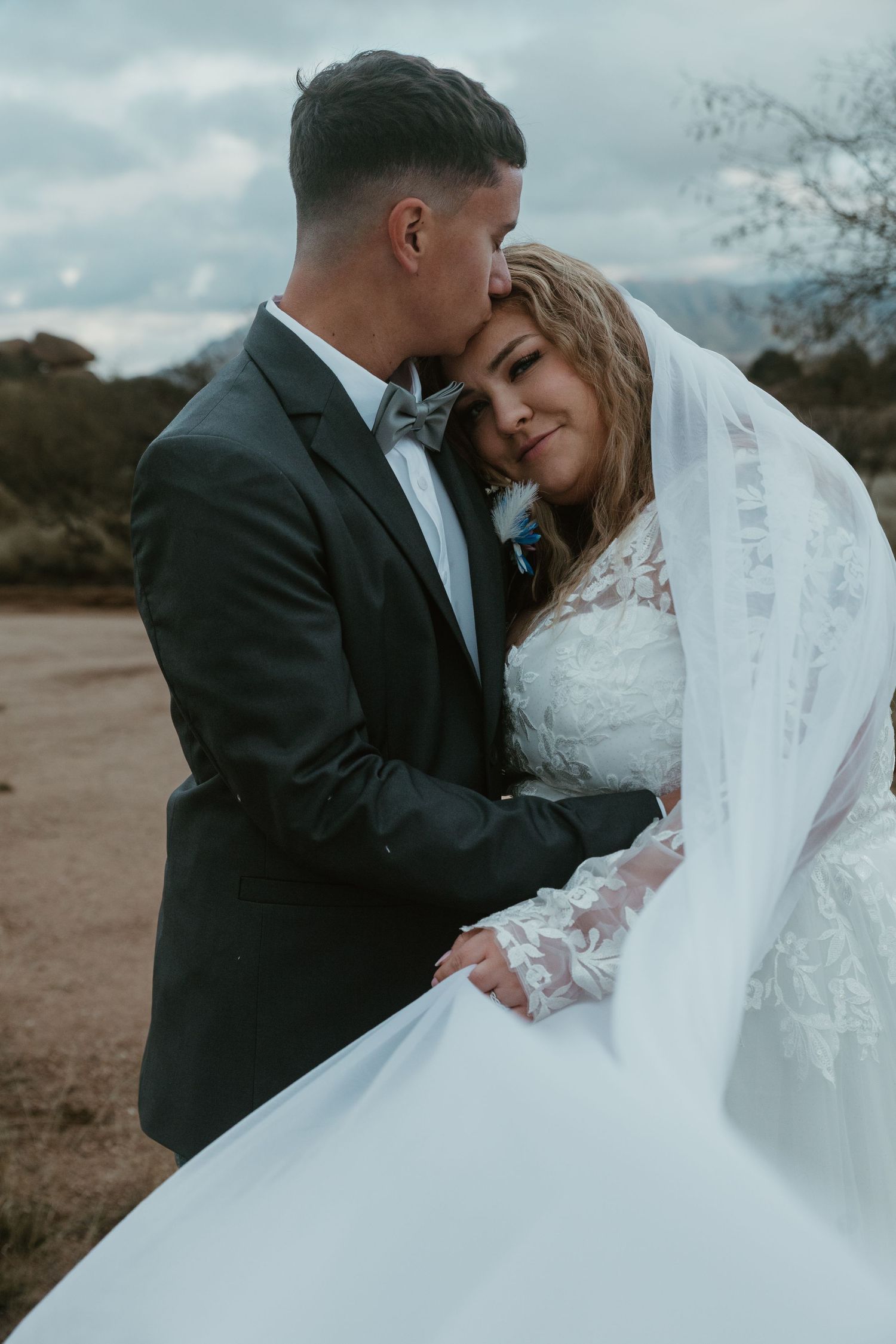 A tender moment between newlyweds outdoors, with the bride in a lace white gown and veil, and groom in dark suit. Tucson Wedding photographe