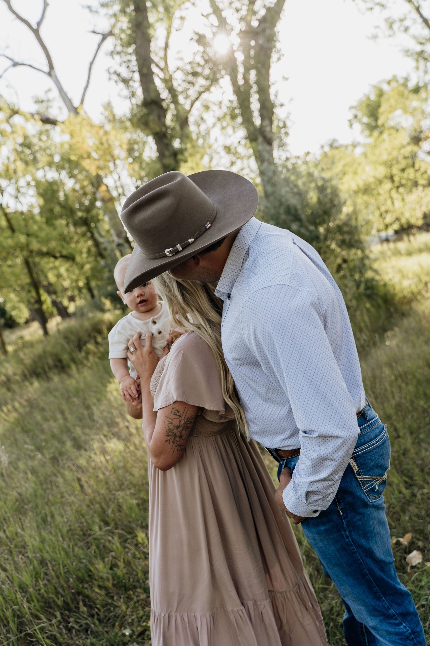 Romantic couple sharing a kiss outdoors, man in cowboy hat embracing blonde woman in pink dress.