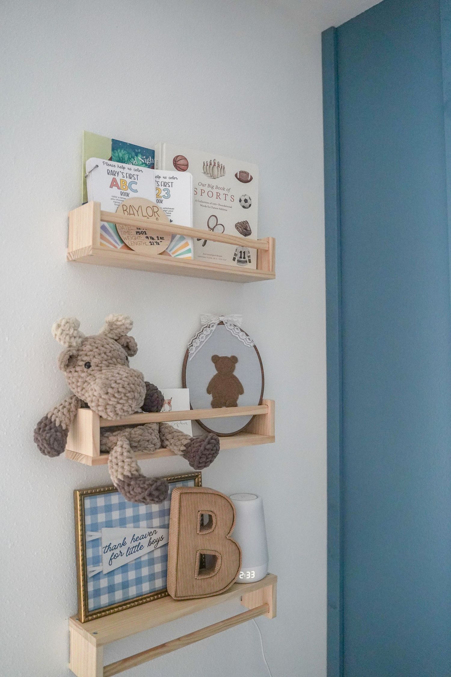 Nursery wall shelves decorated with stuffed moose, books, bear frame, and letter B decor.