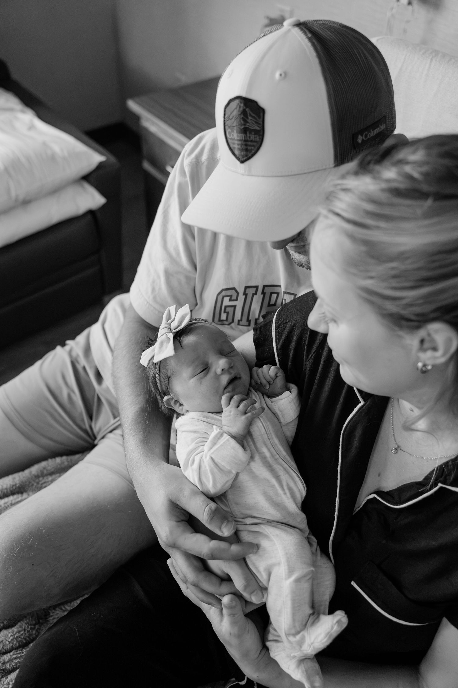 Black and white photo of new parents lovingly gazing at their sleeping newborn in hospital.