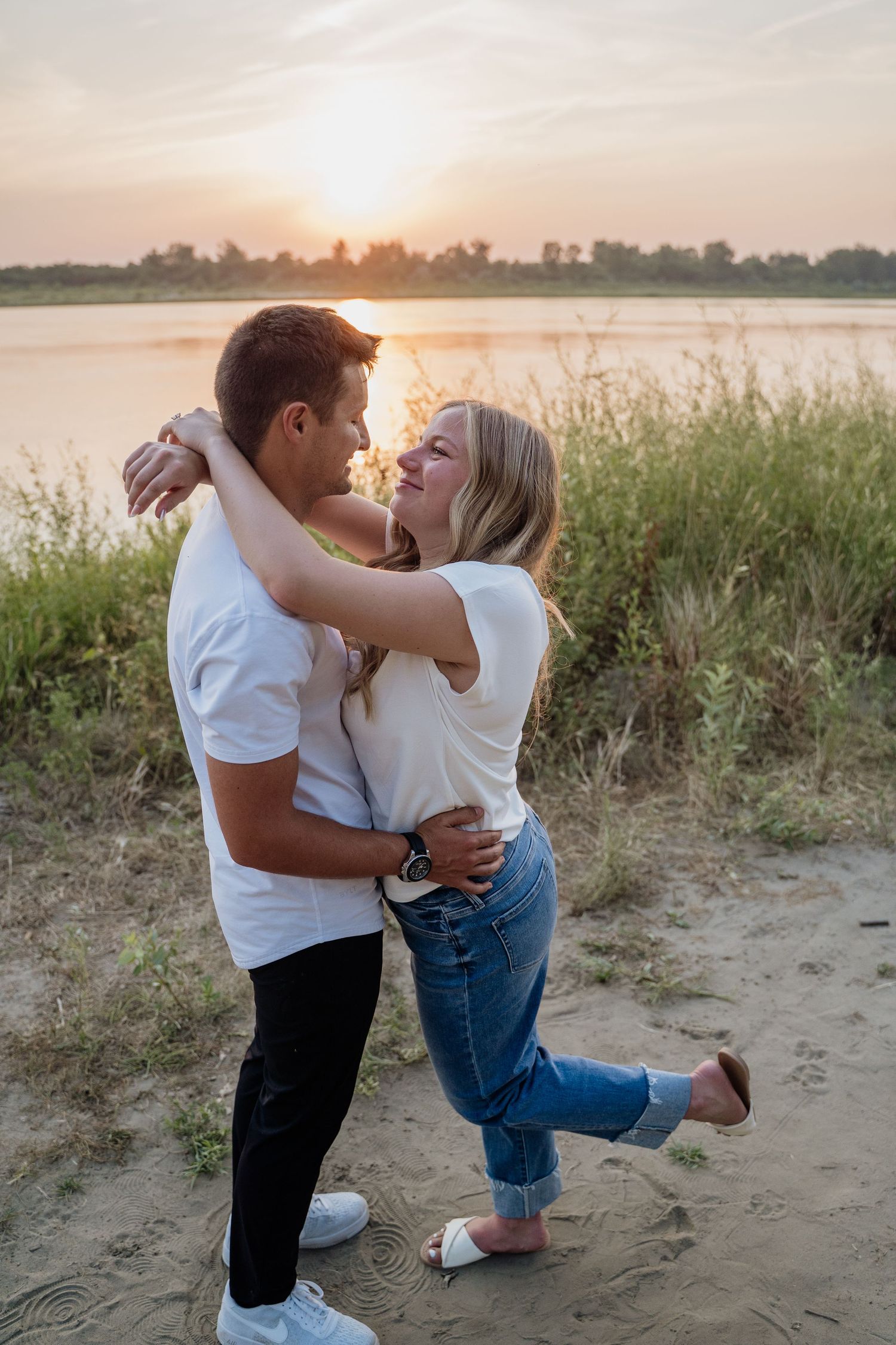 A happy couple embraces and nearly kisses on a sandy beach at golden sunset.