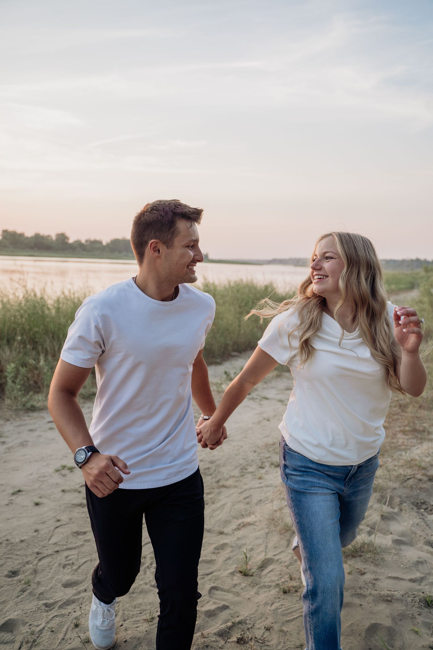 A joyful couple holds hands and runs along a sandy beach at sunset, laughing together.