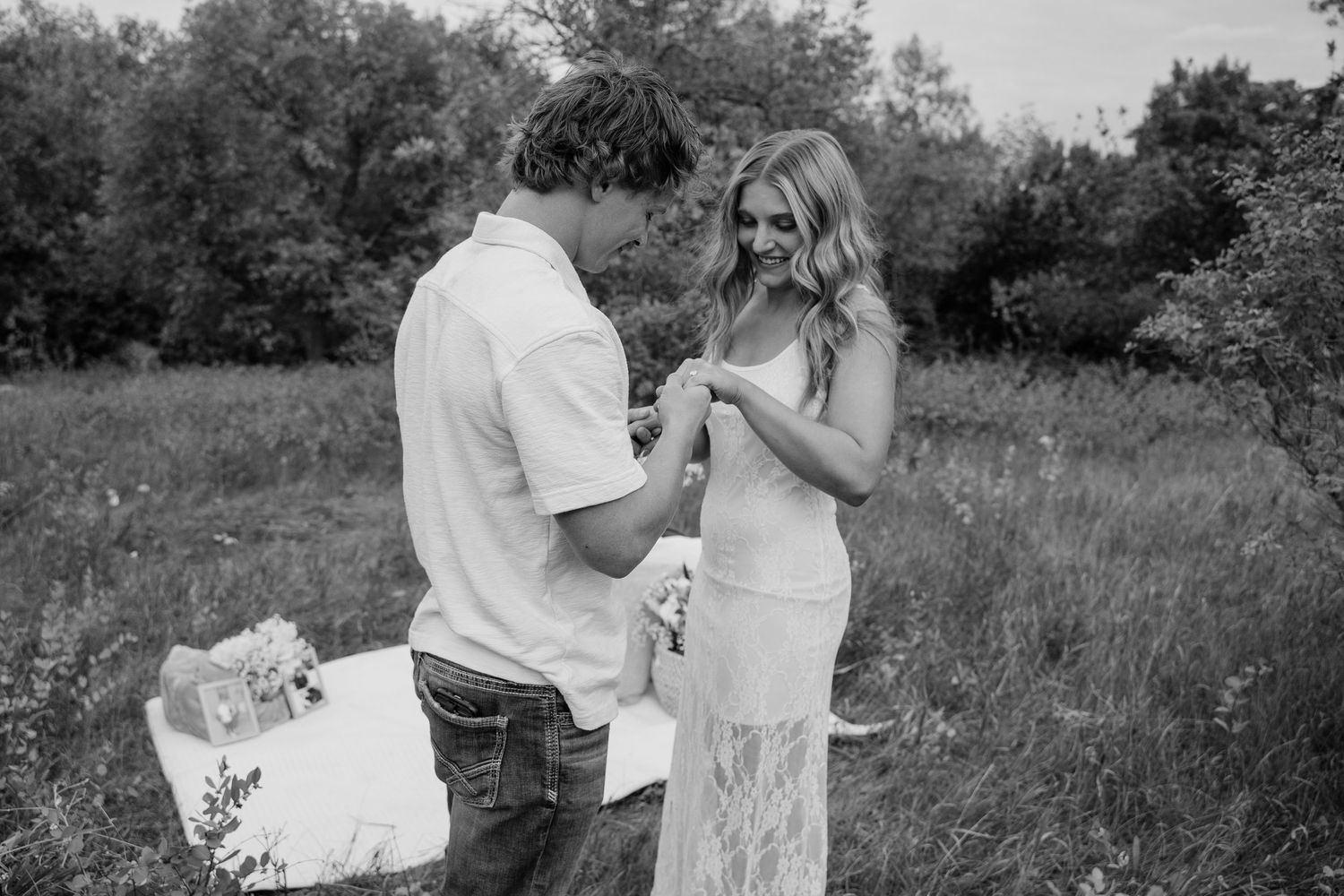 Black and white photo of a couple sharing a romantic moment in a sunlit meadow during an outdoor proposal.