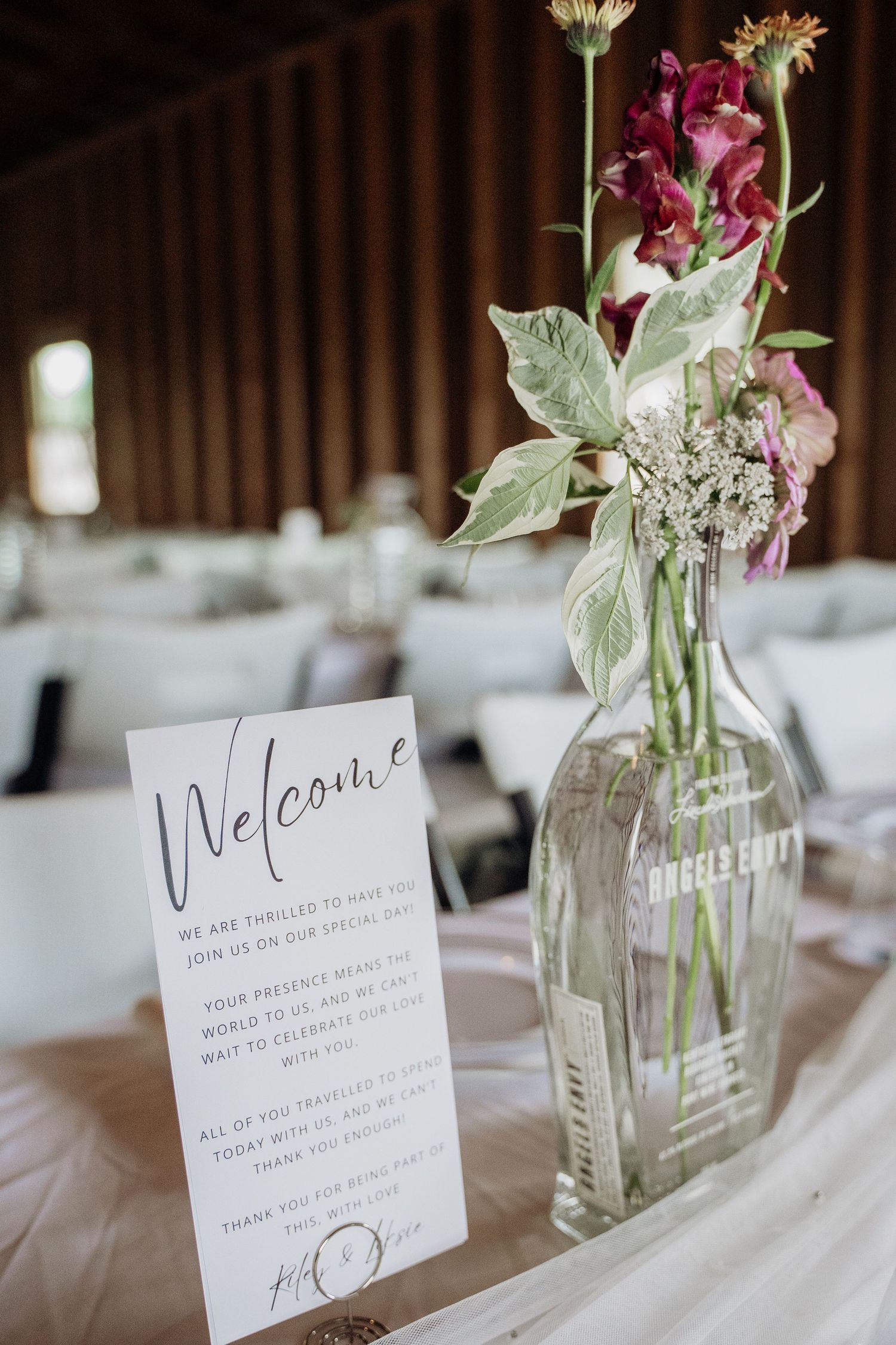 Wedding welcome sign beside wildflower bouquet in glass bottle vase at reception.
