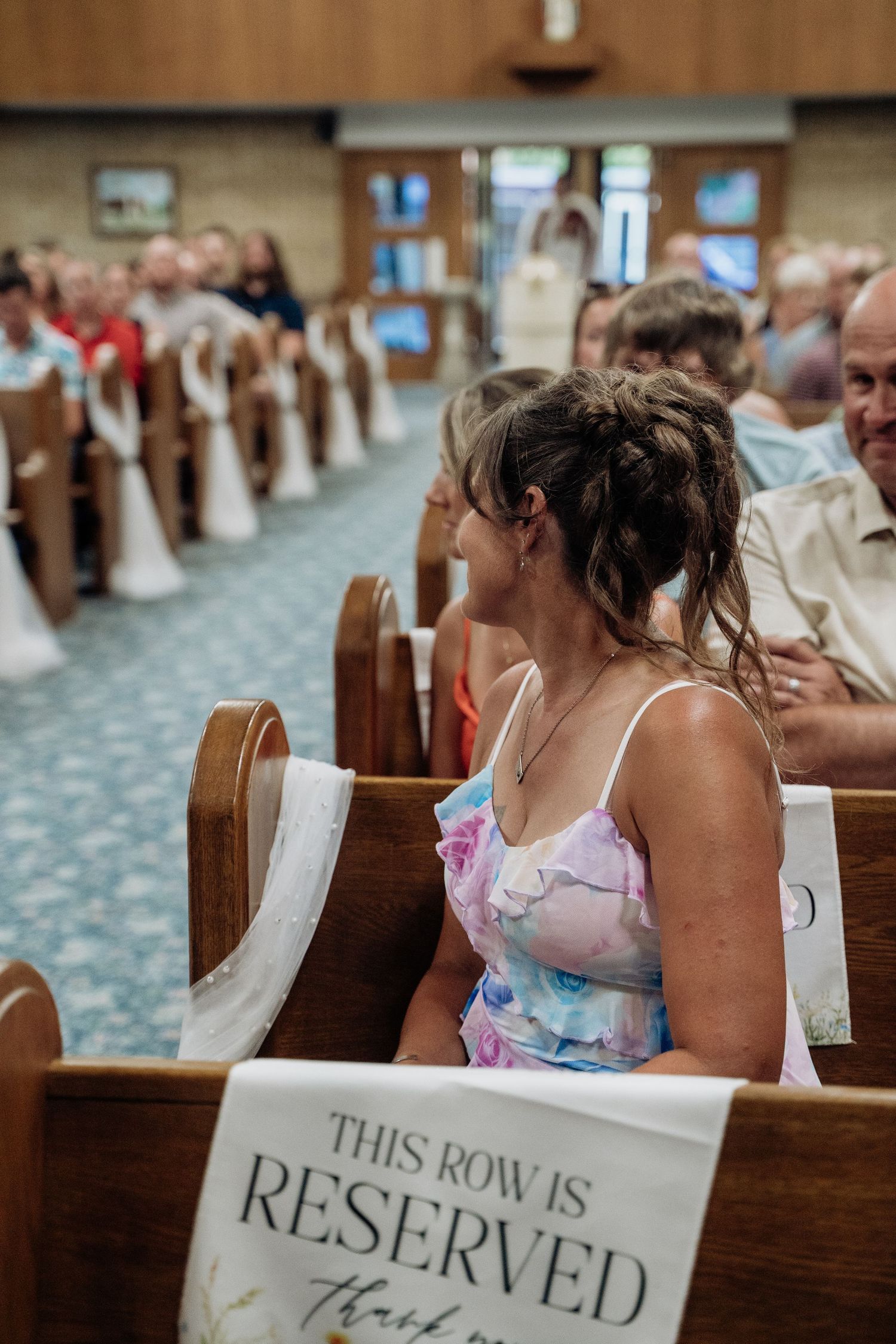 Wedding guests seated in church pews with reserved row sign during ceremony.