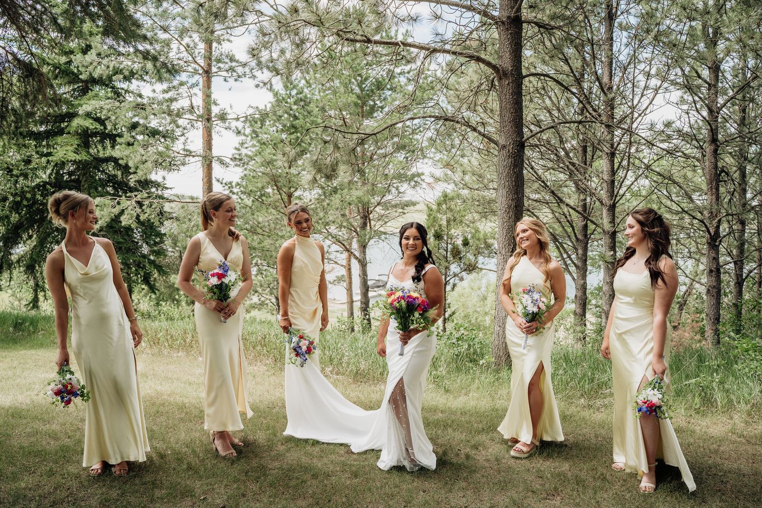Bride and bridesmaids in cream dresses walking through a lush green forested area.