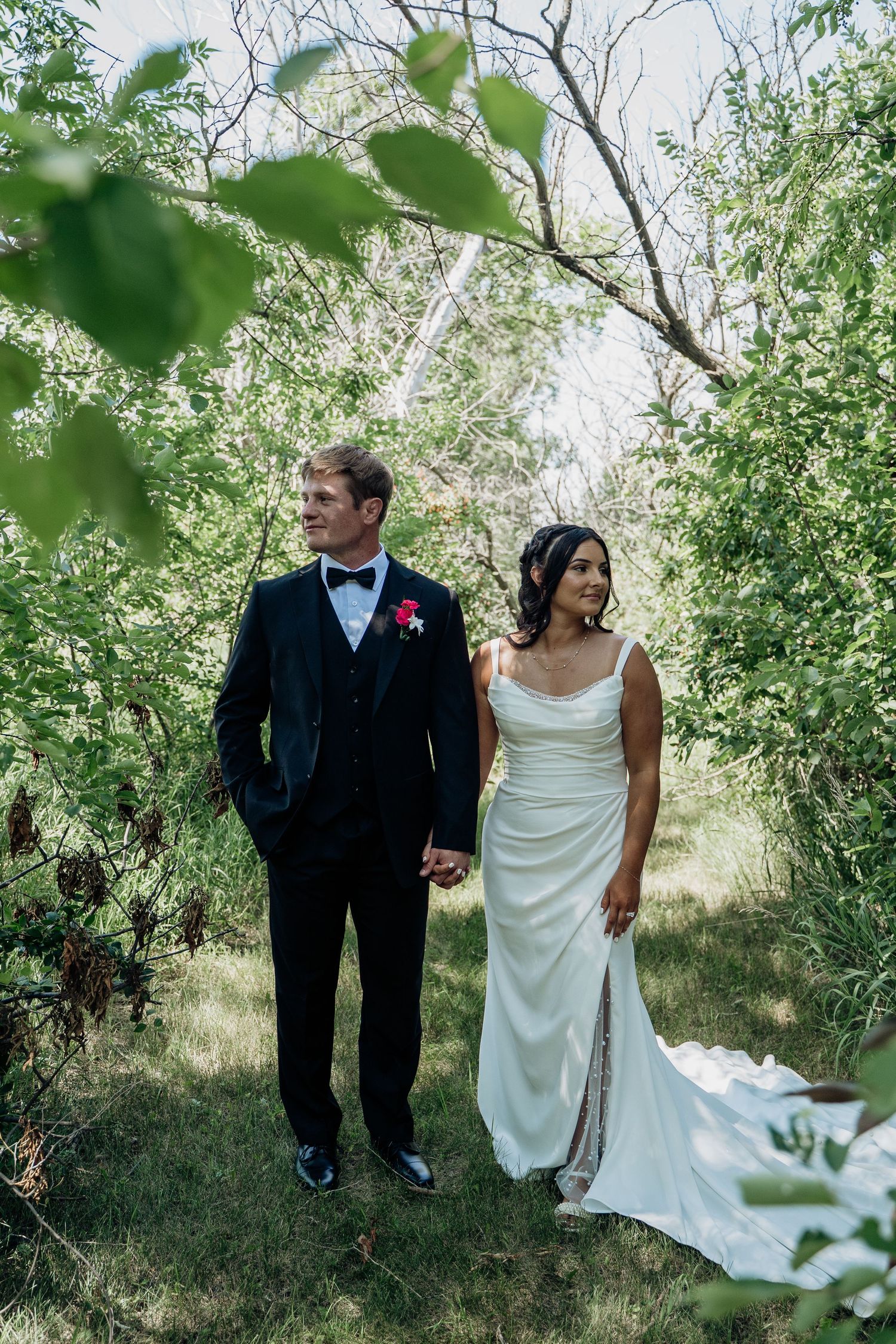 Bride and groom walking hand in hand through a lush green wooded area on their wedding day.