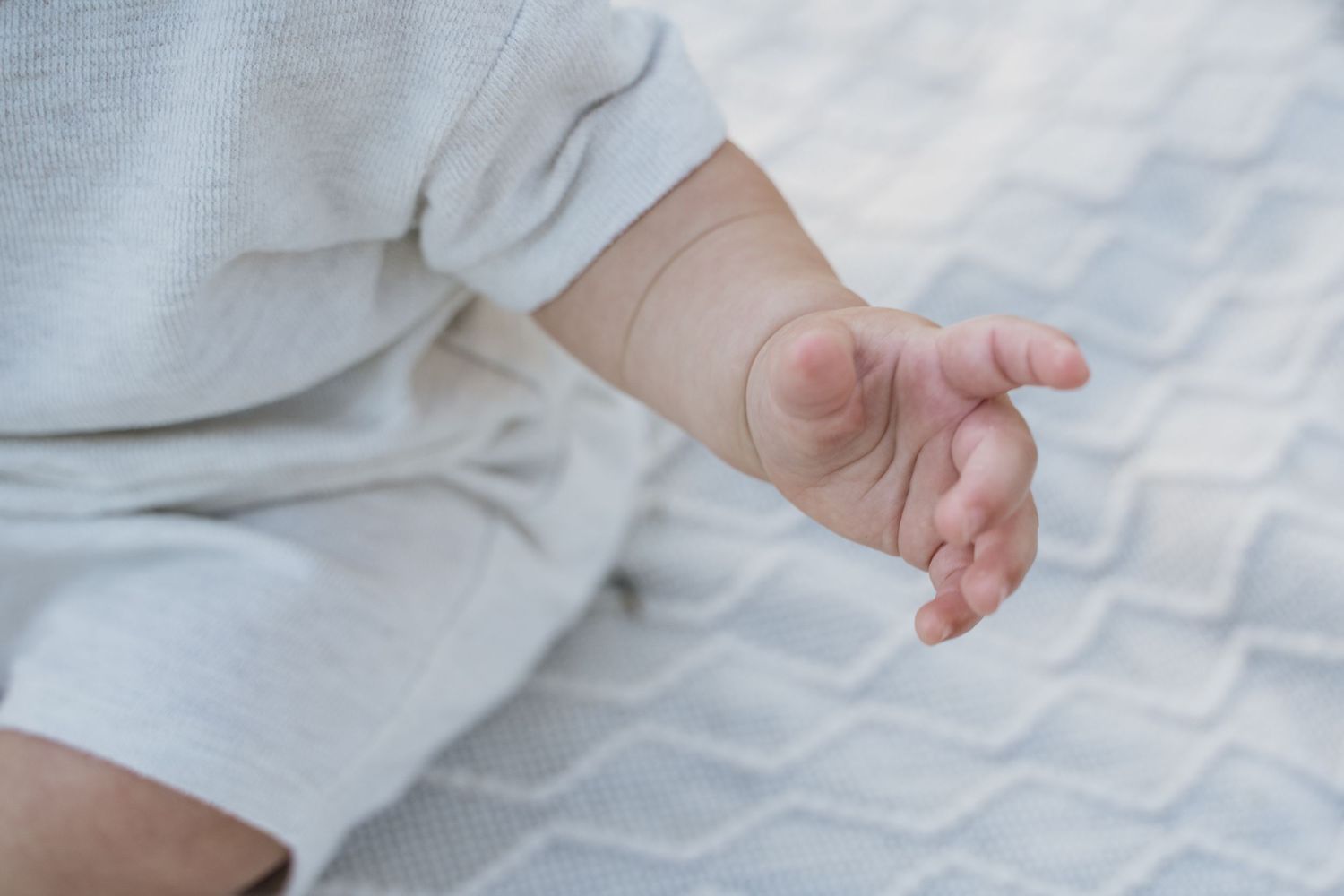 Close-up of a newborn baby's tiny hand resting on a soft white textured blanket.