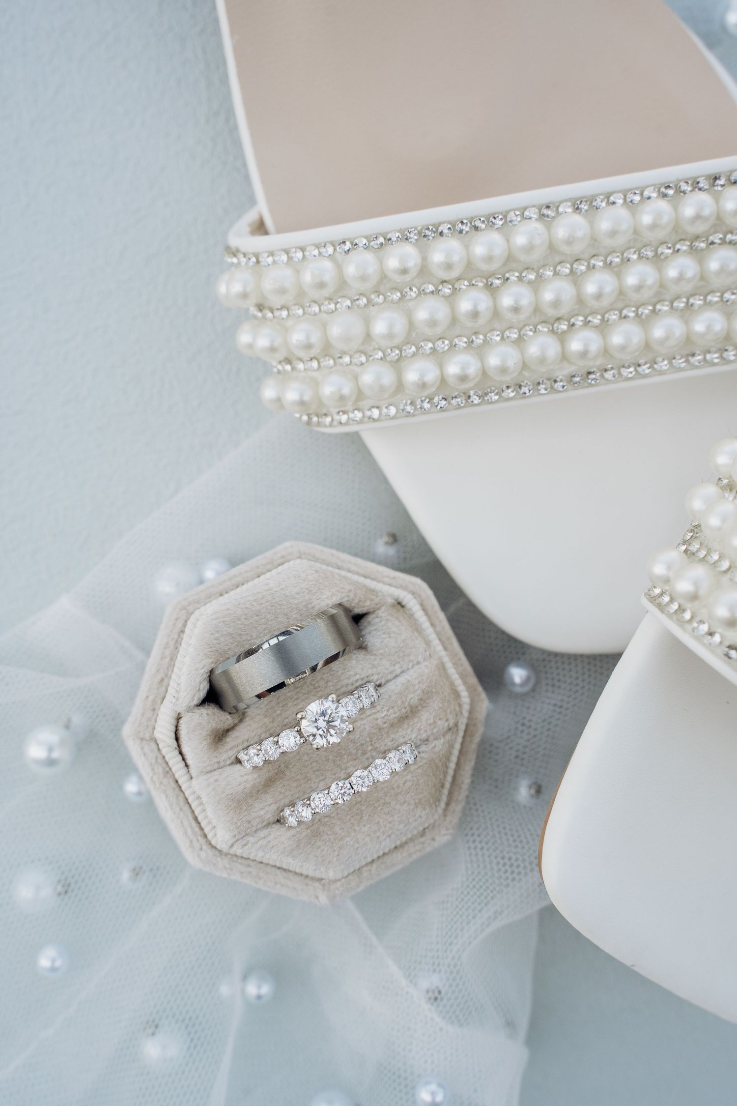 Diamond engagement ring and wedding band displayed in a velvet hexagon box with pearl-adorned jewelry boxes.